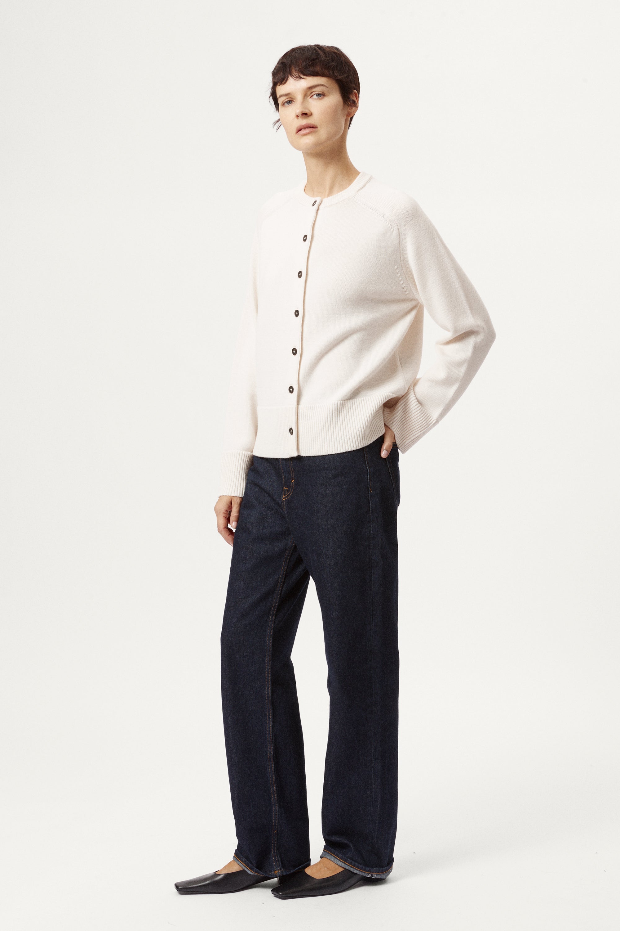 Person wearing a cream cardigan with black buttons on a white background