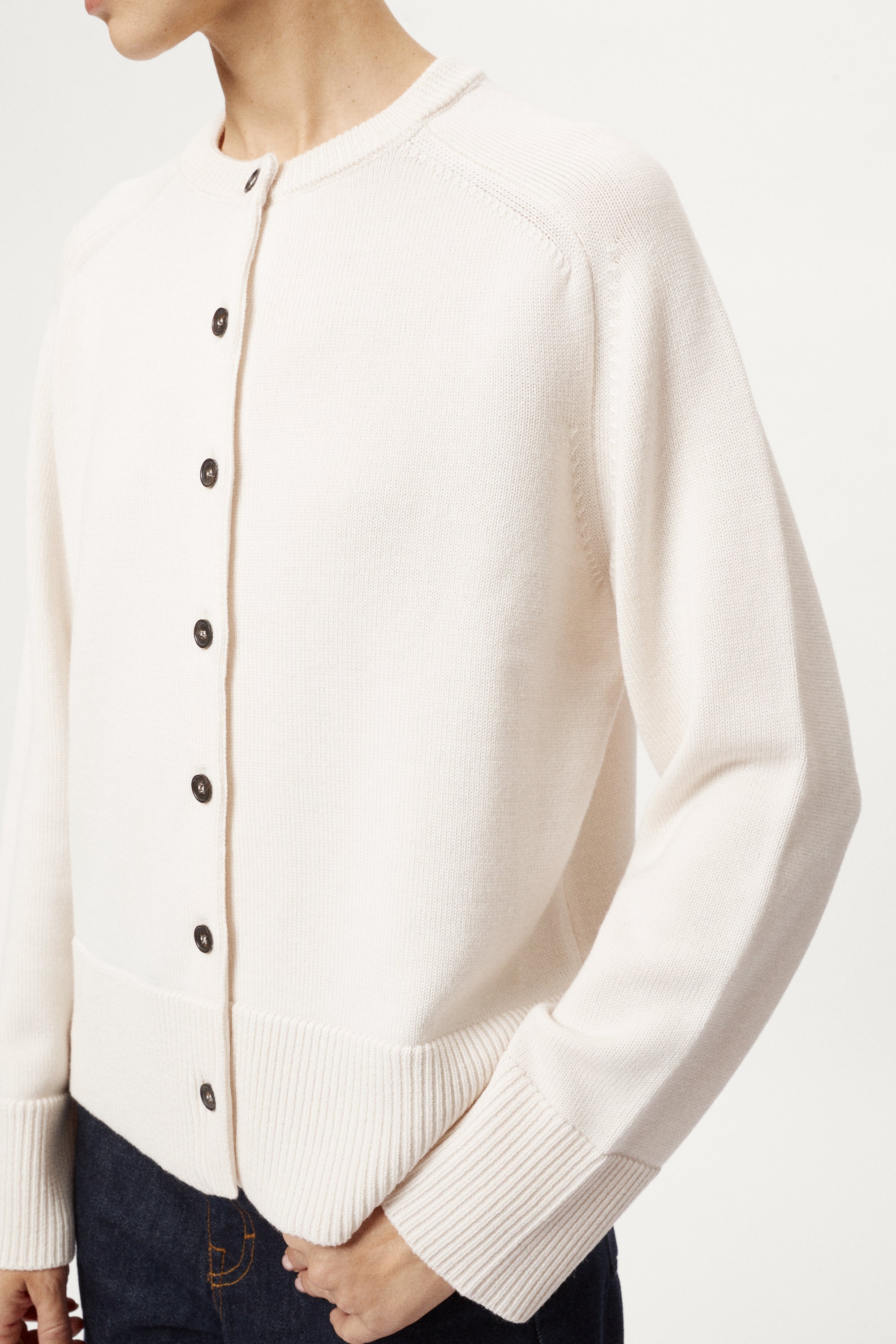 Person wearing a cream cardigan with black buttons on a white background