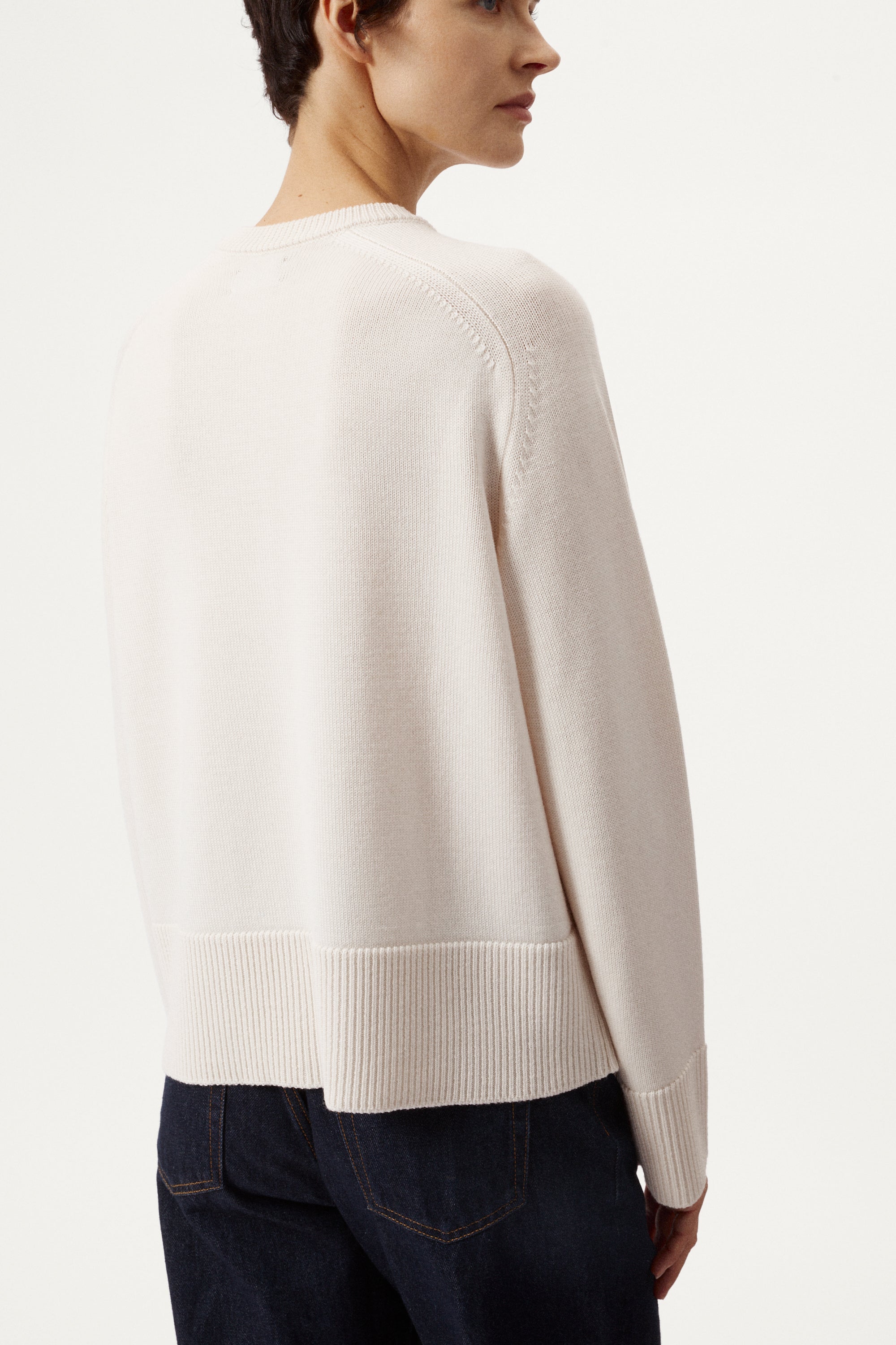 Person wearing a cream cardigan with black buttons on a white background