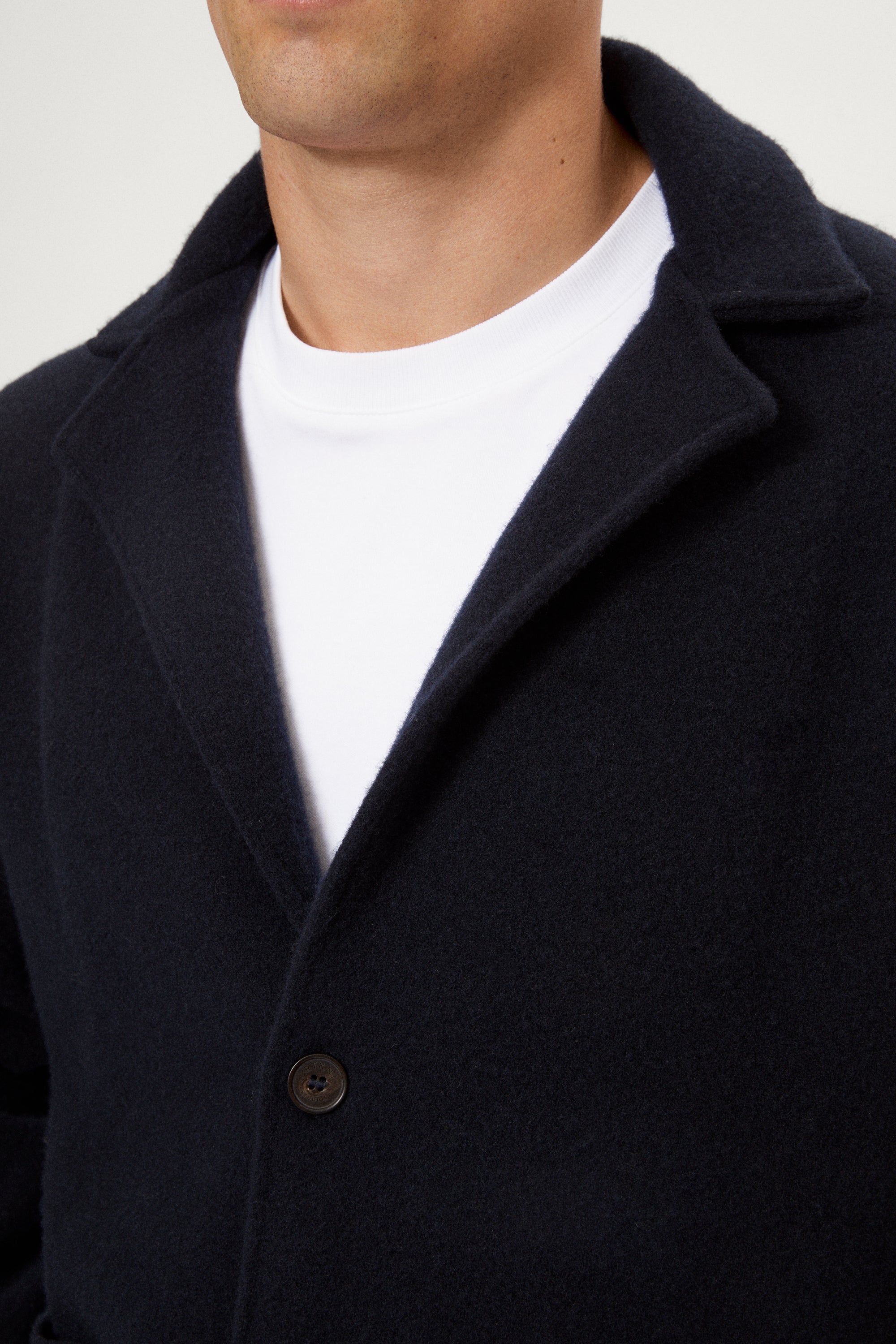 Close-up of a person wearing a dark coat over a white shirt against a neutral background