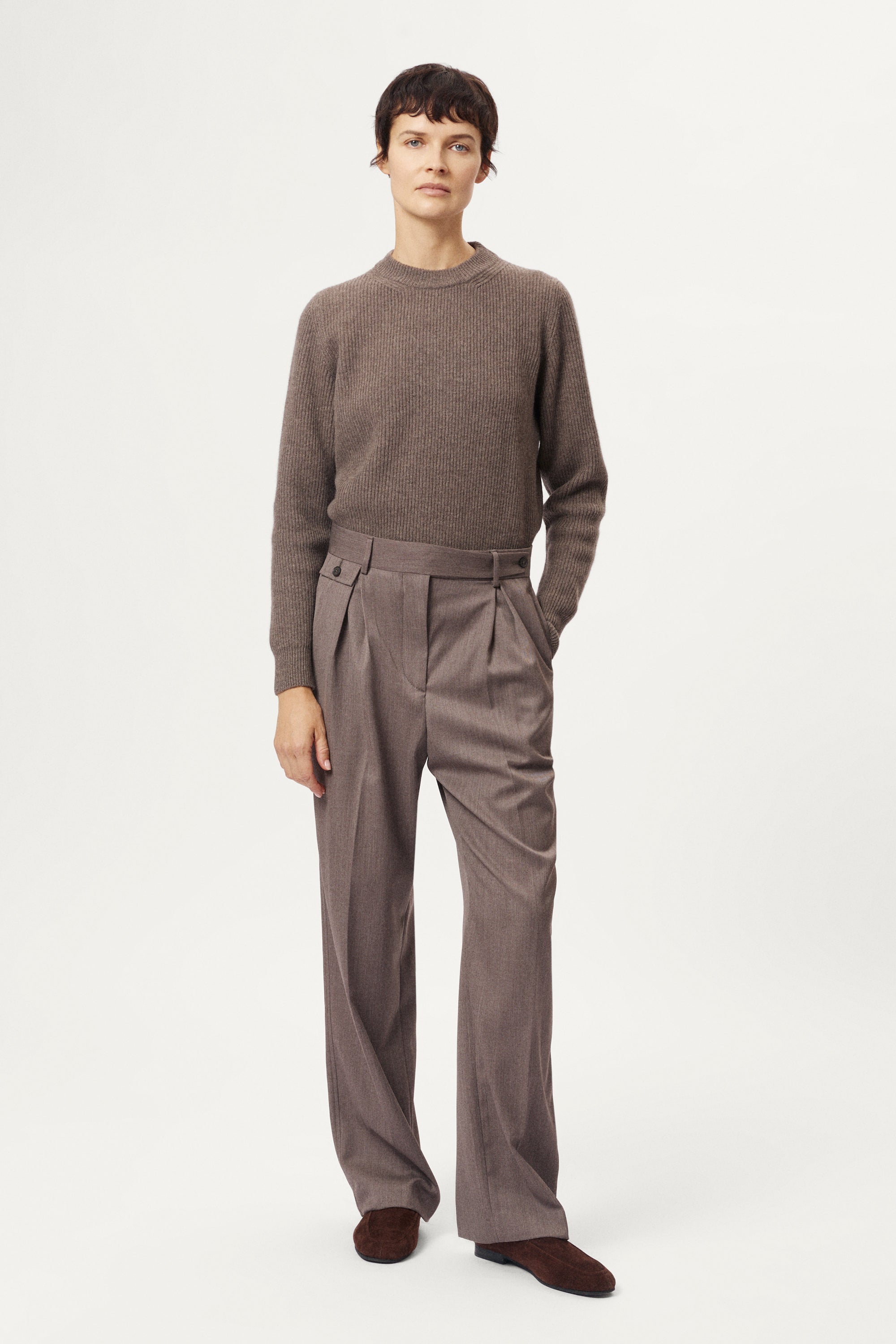 Brown pleated pants worn by a person on a white background