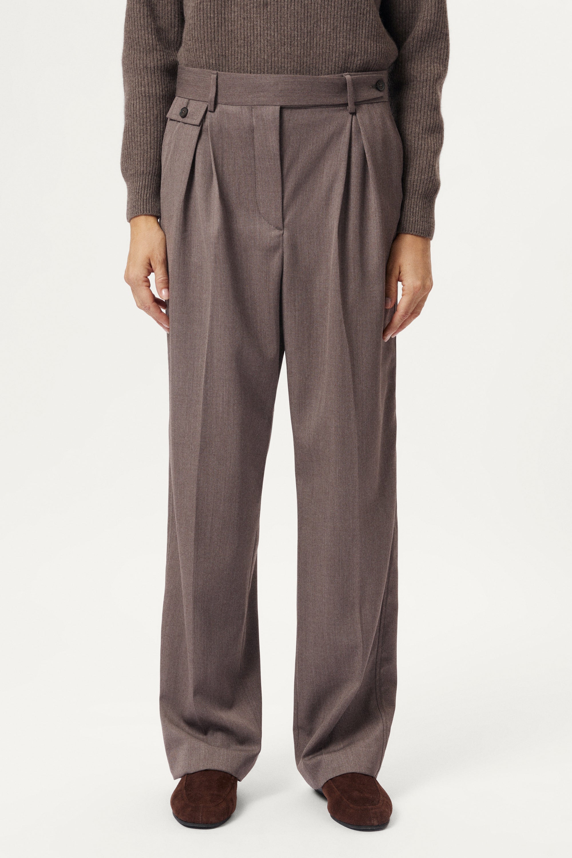 Brown pleated pants worn by a person on a white background
