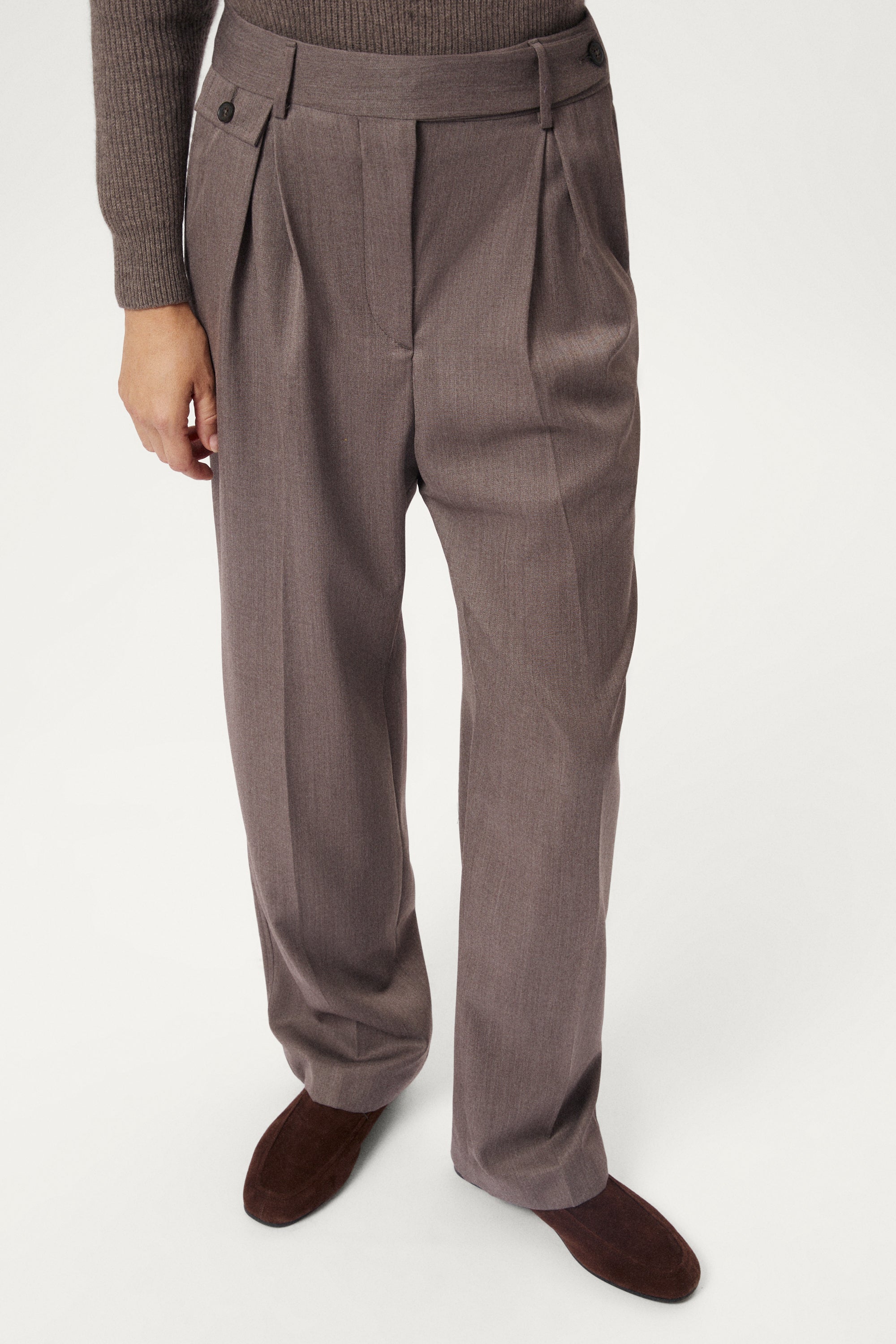 Brown pleated pants worn by a person on a white background
