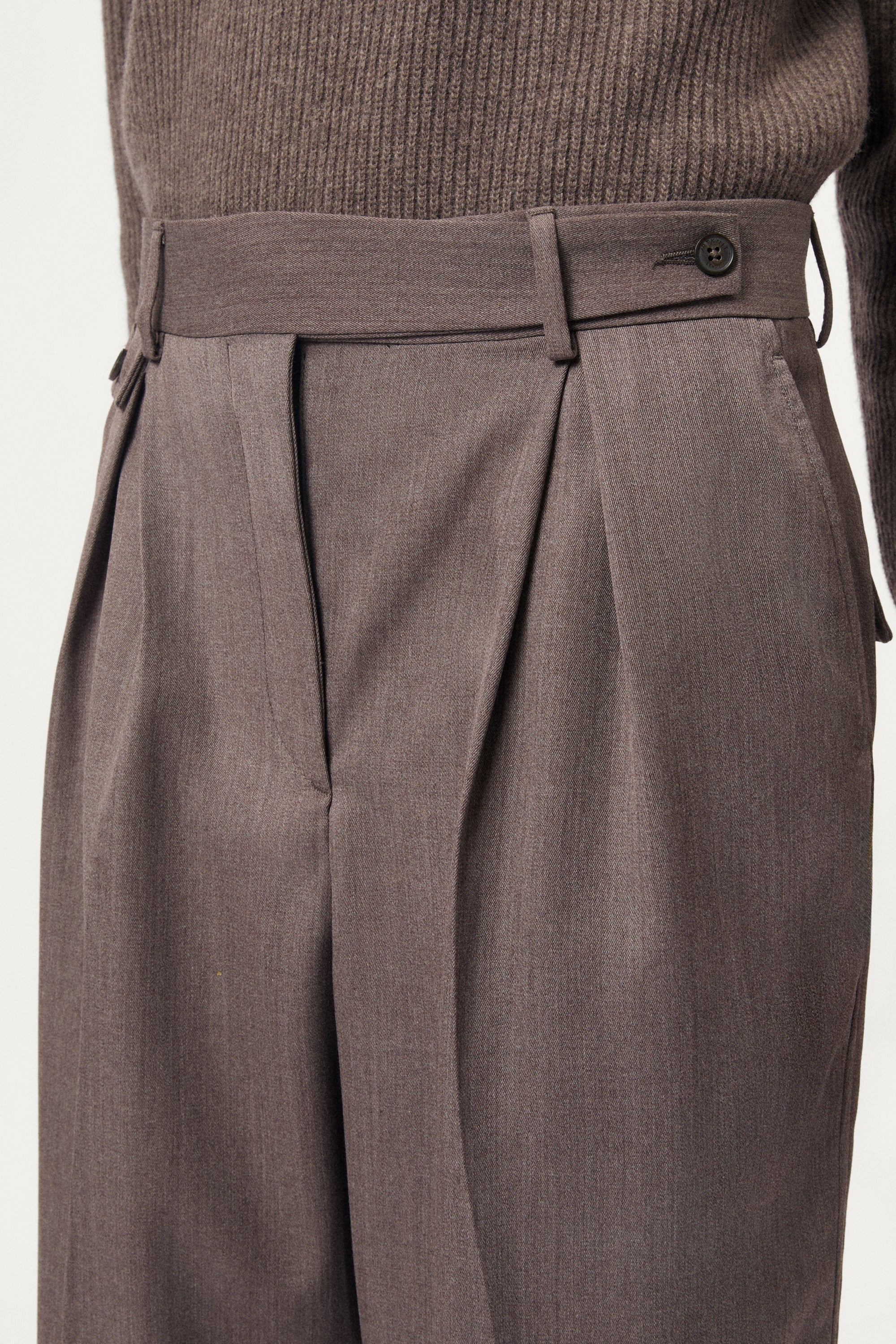 Close-up of brown pleated pants with a button on a plain background