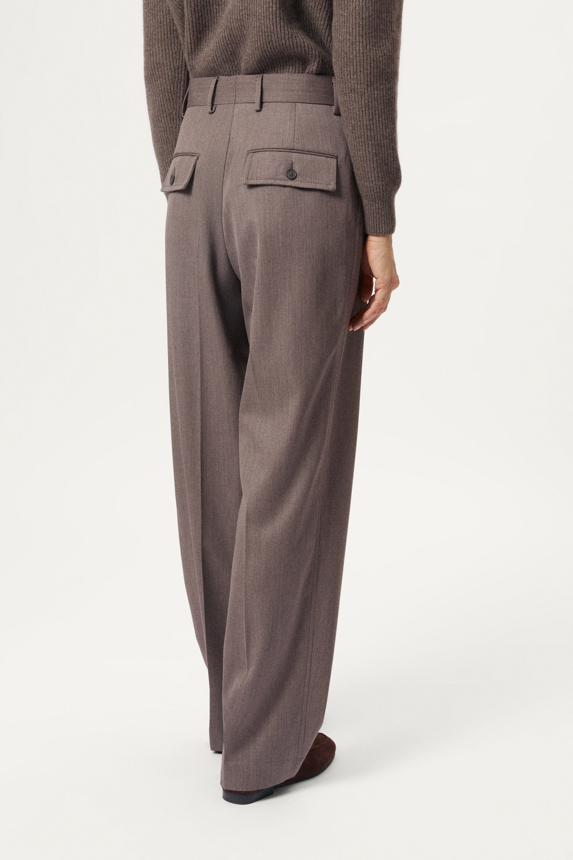 Brown pleated pants worn by a person on a white background