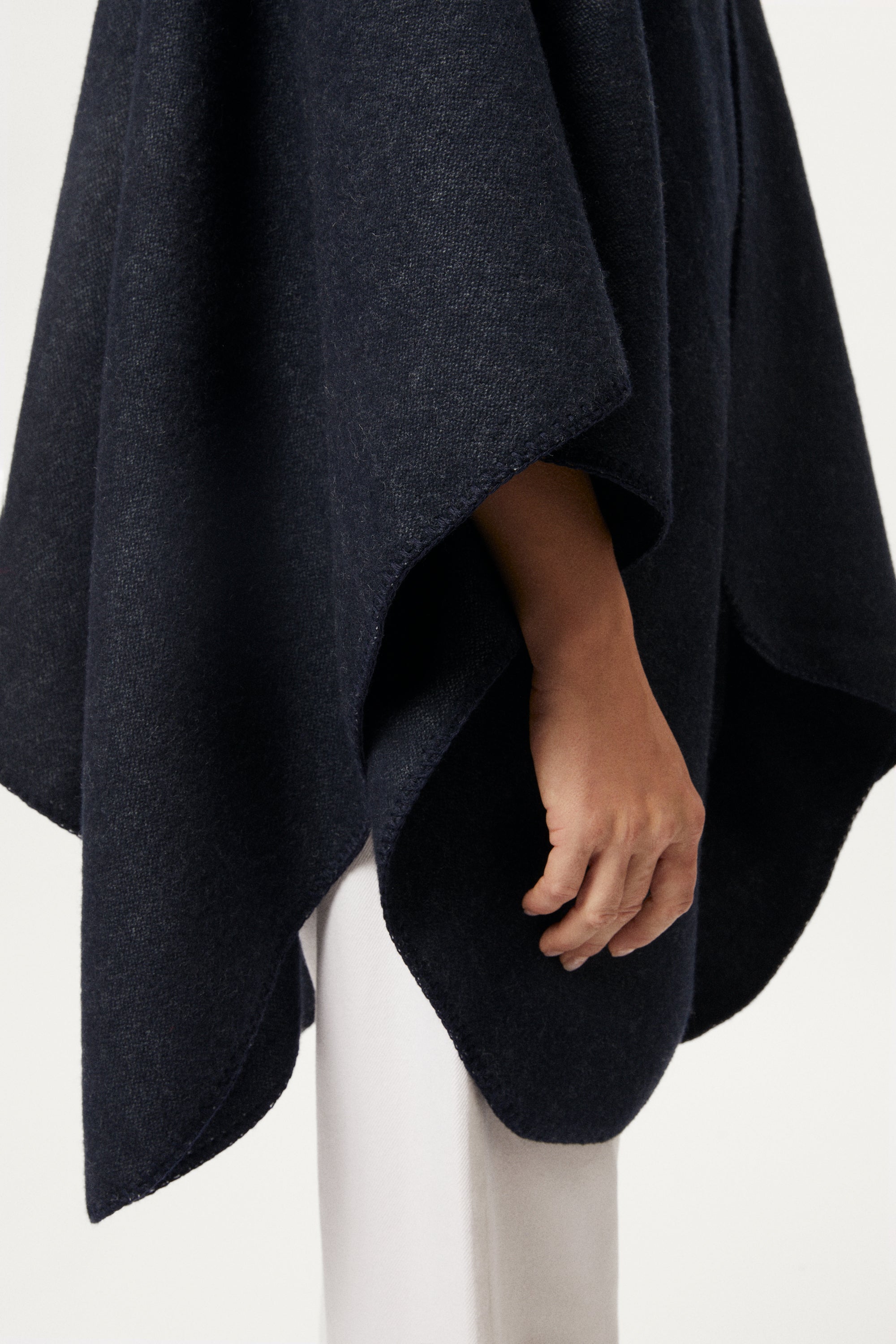 woman wearing a blue navy poncho over a turtleneck and white pants on a white background