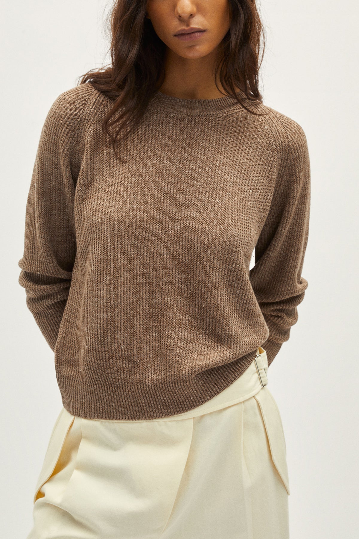 Woman wearing a brown sweater and white pants on a white background