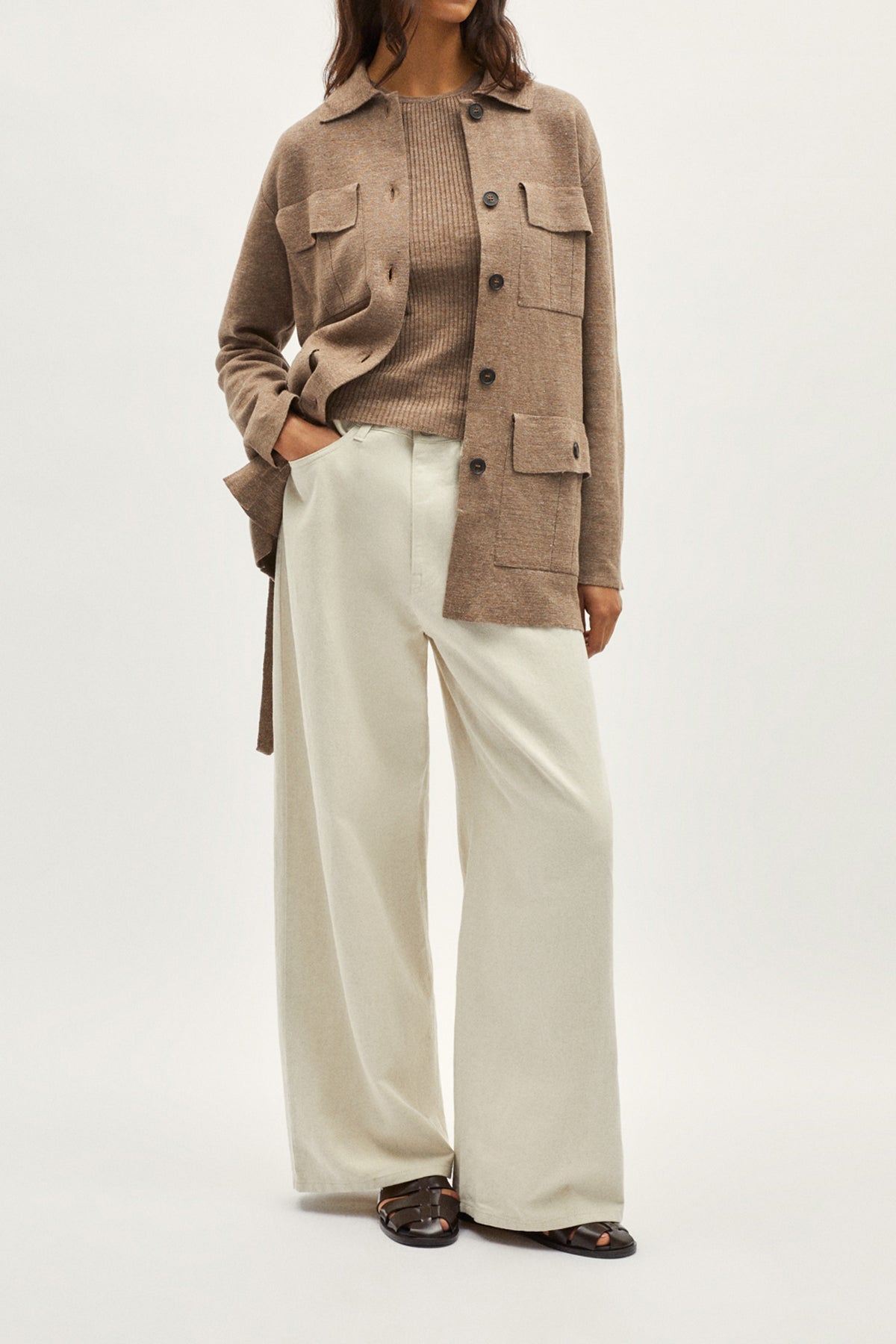 Person wearing a brown jacket and white pants on a plain background