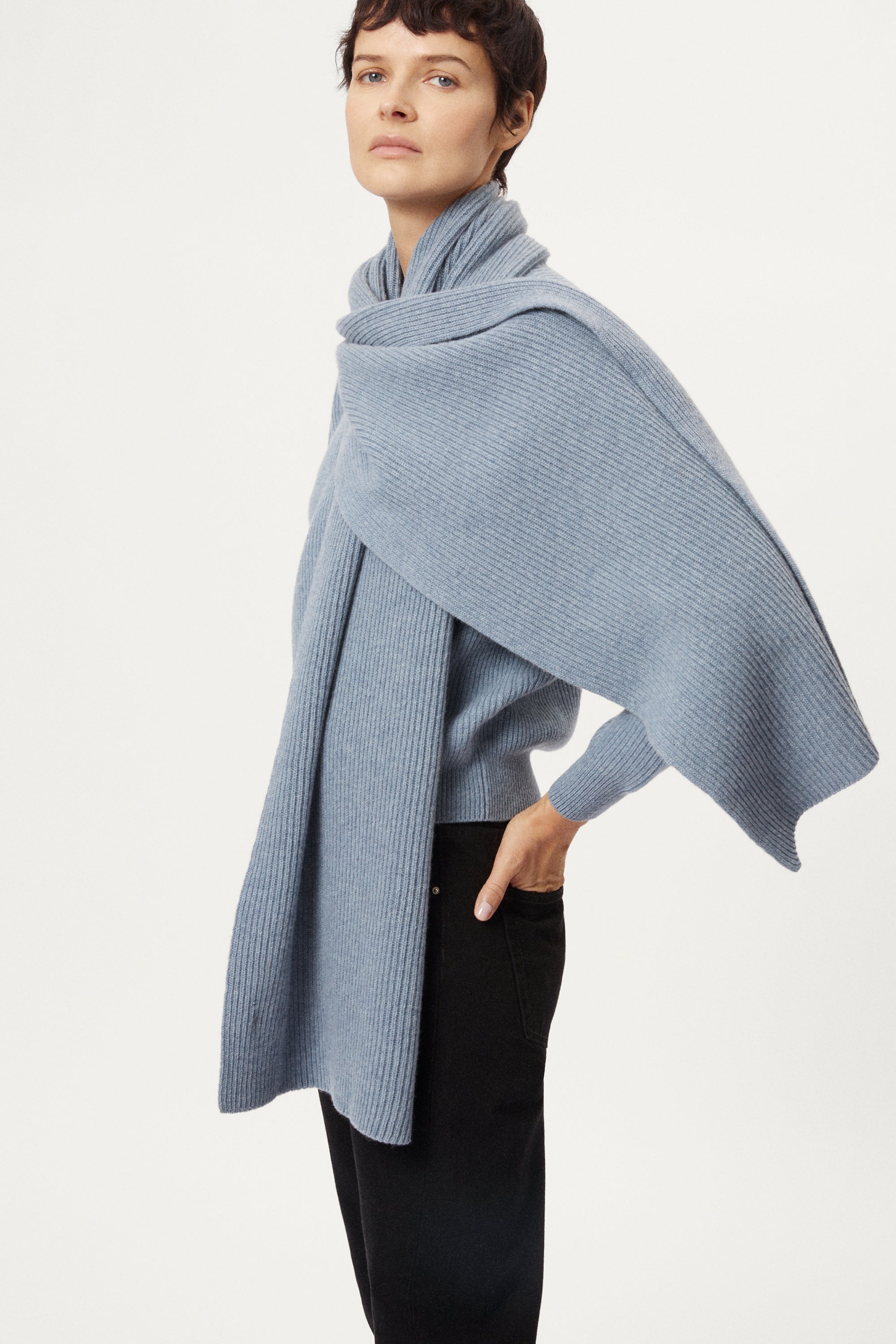 Woman wearing a ash blue woolen scarf over his shoulders against a plain background