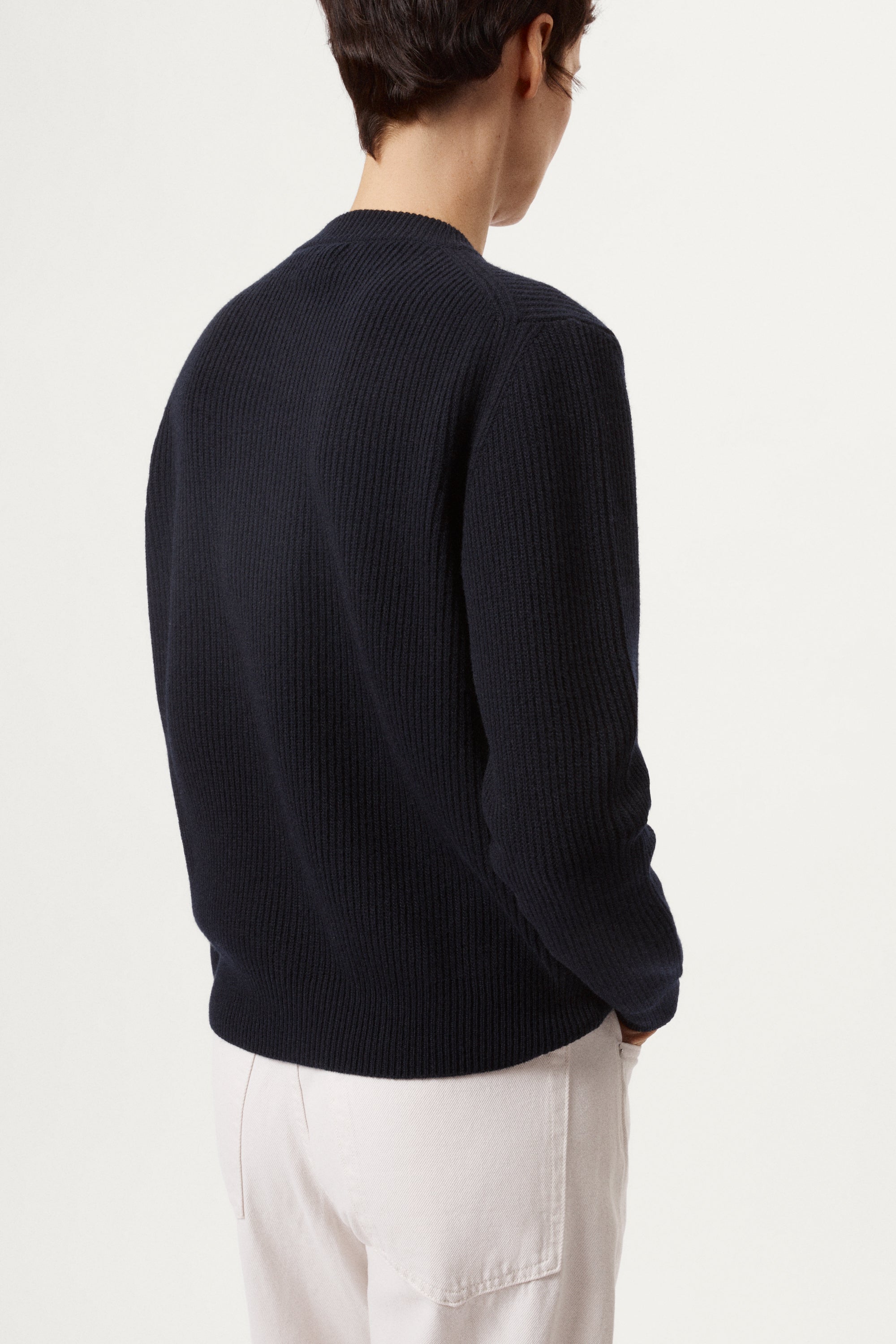 woman wearing a blue navy woolen sweater and white pants against a light background