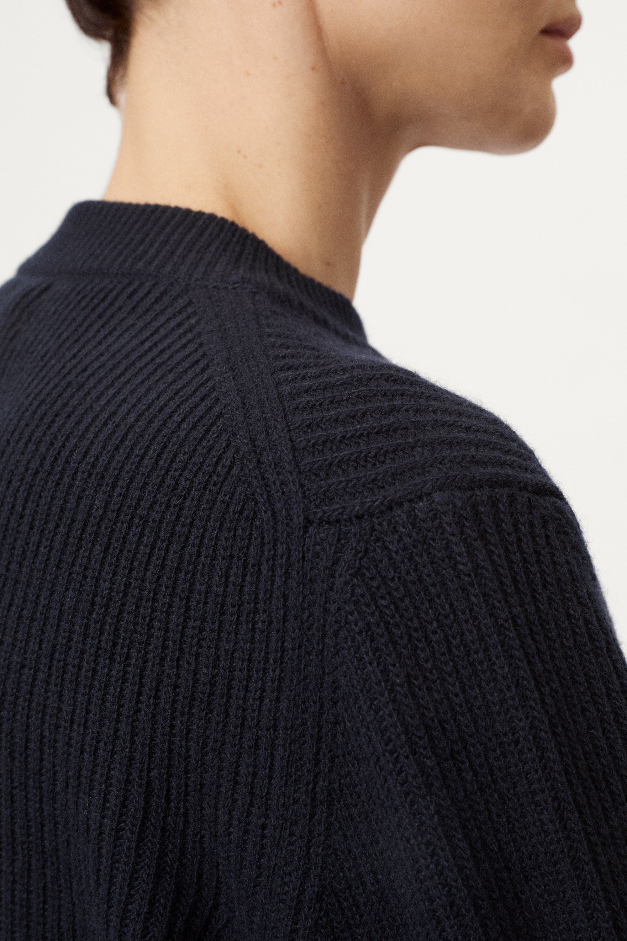 Close-up of a person wearing a dark blue ribbed sweater on a light gray background