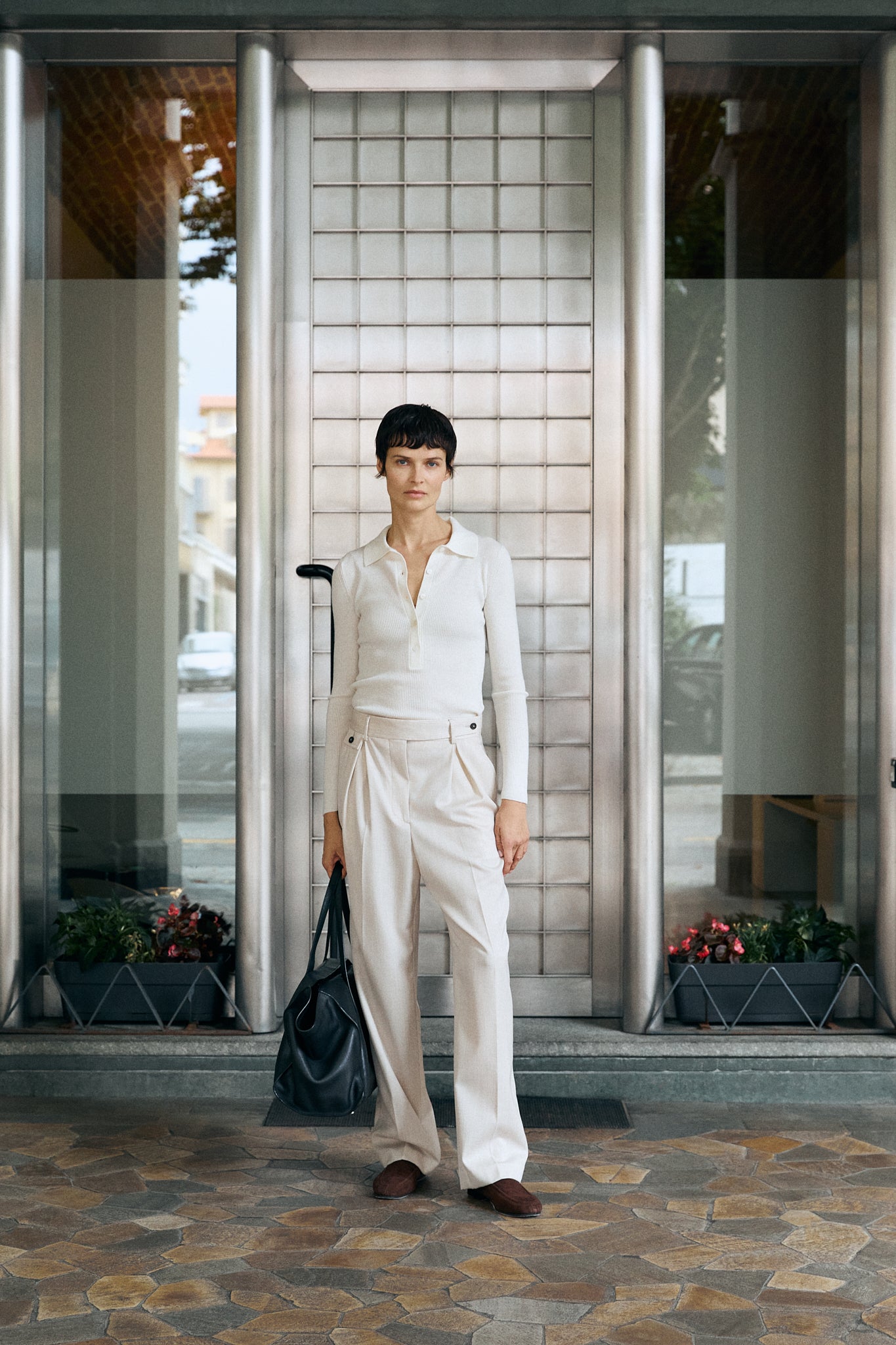 Person in a white outfit standing in front of a glass door with a suitcase.