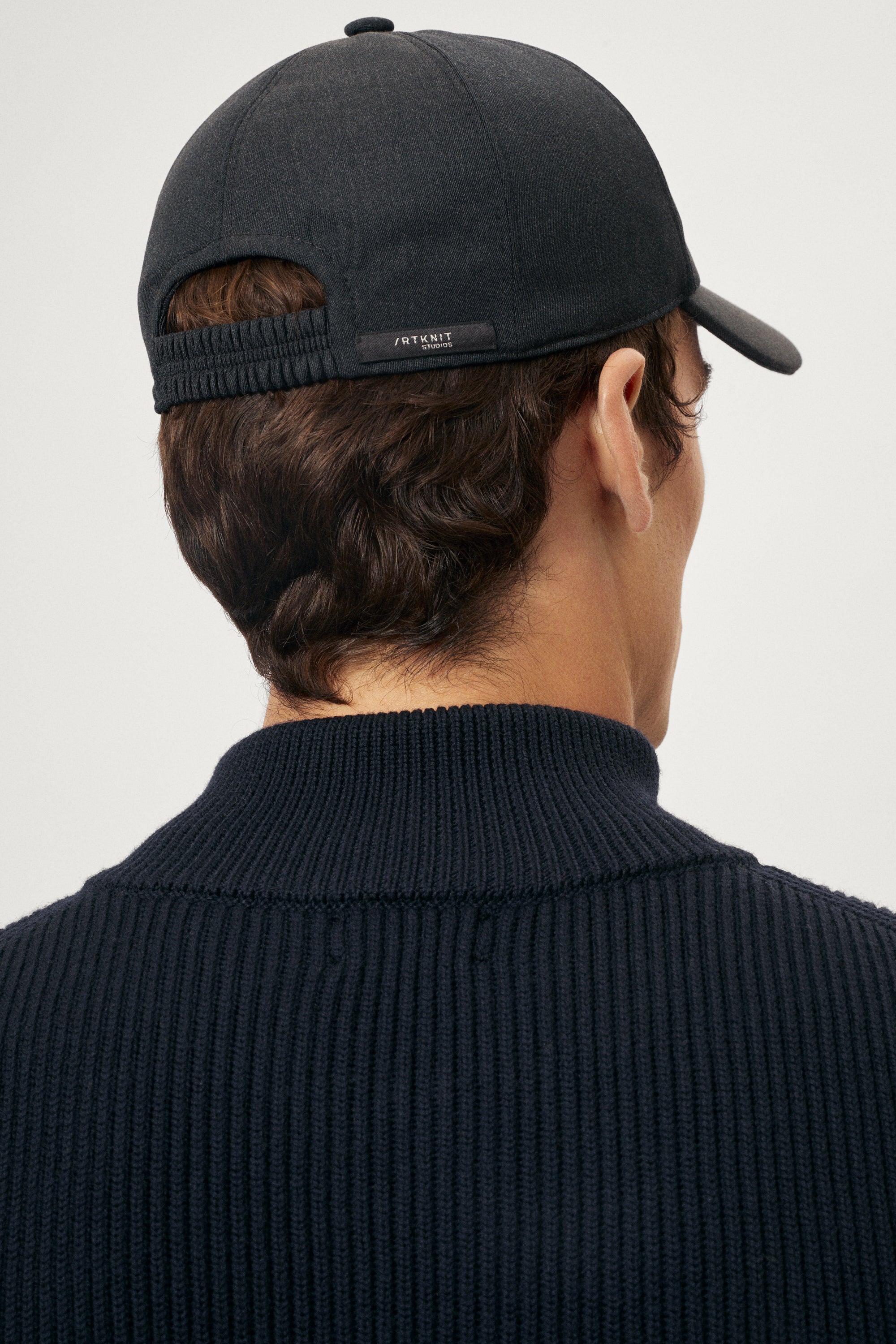 man wearing a dark grey cap and sweater on a light gray background