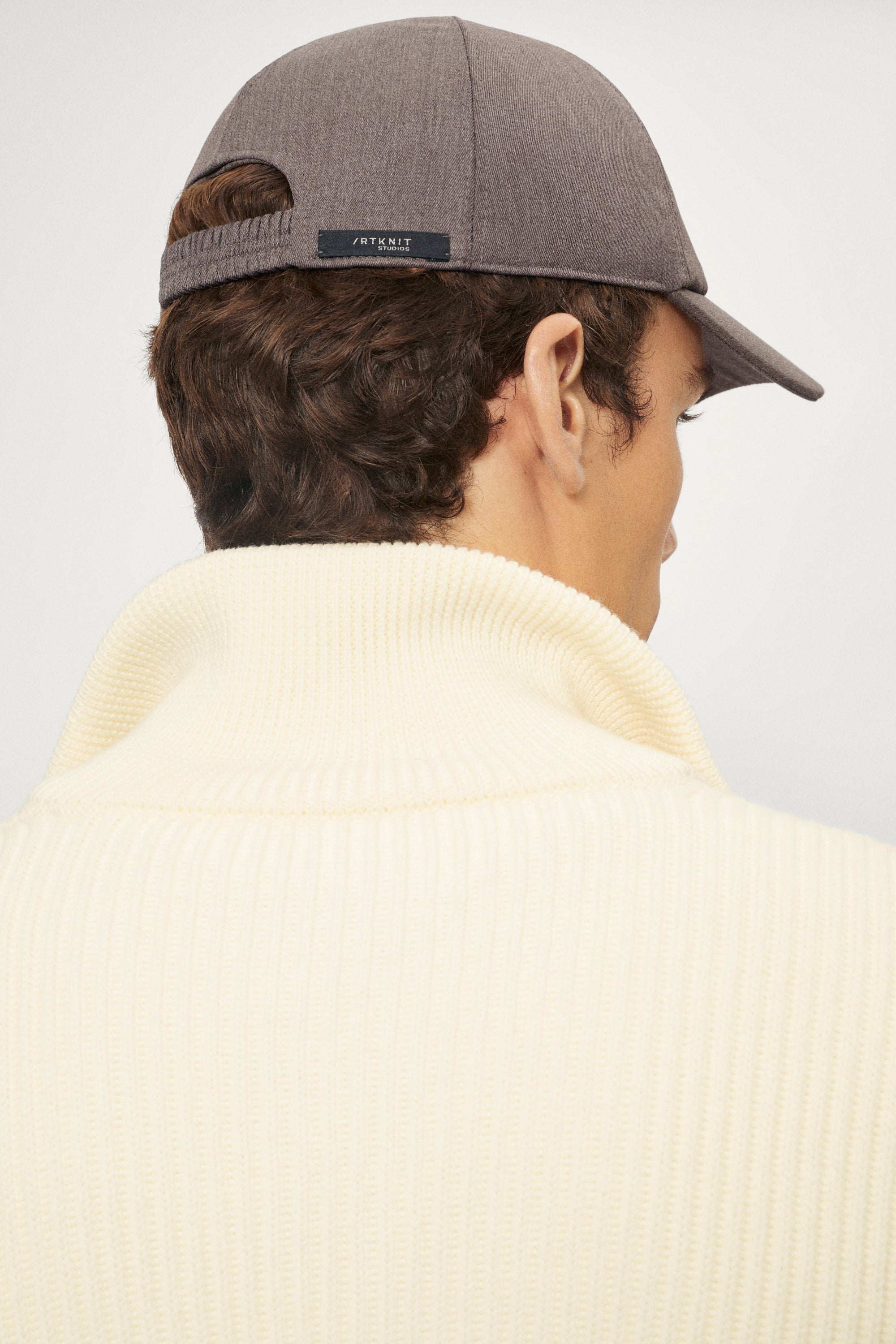 Person wearing a taupe hat with a logo on a plain background