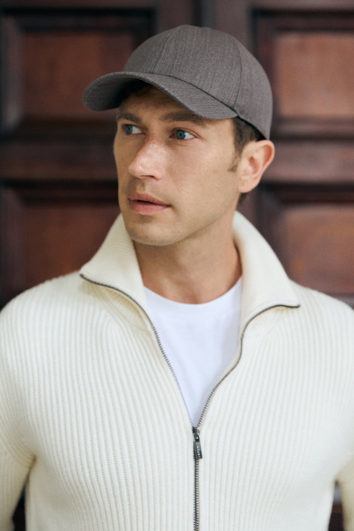 Man wearing a taupe hat and beige high-neck sweater against a city background