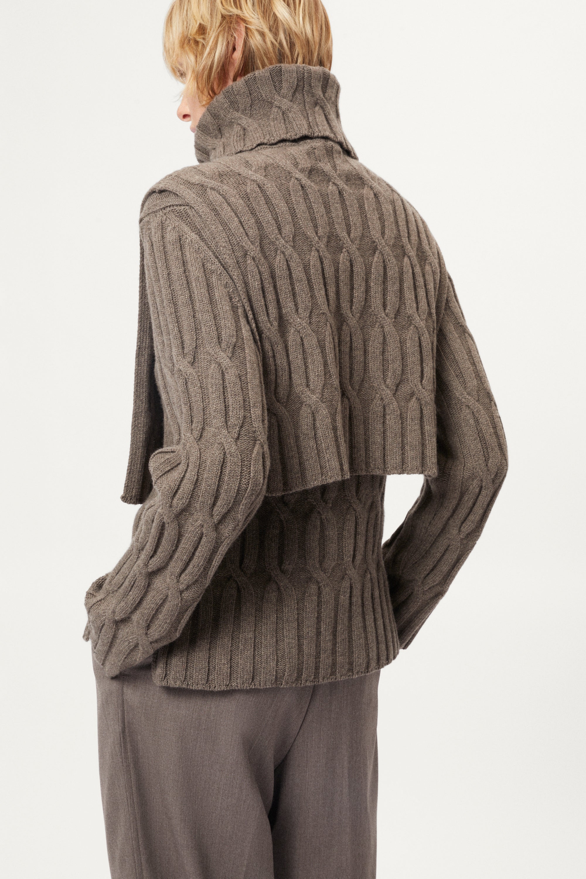 Woman wearing a brown cable knit bib and pants on a white background