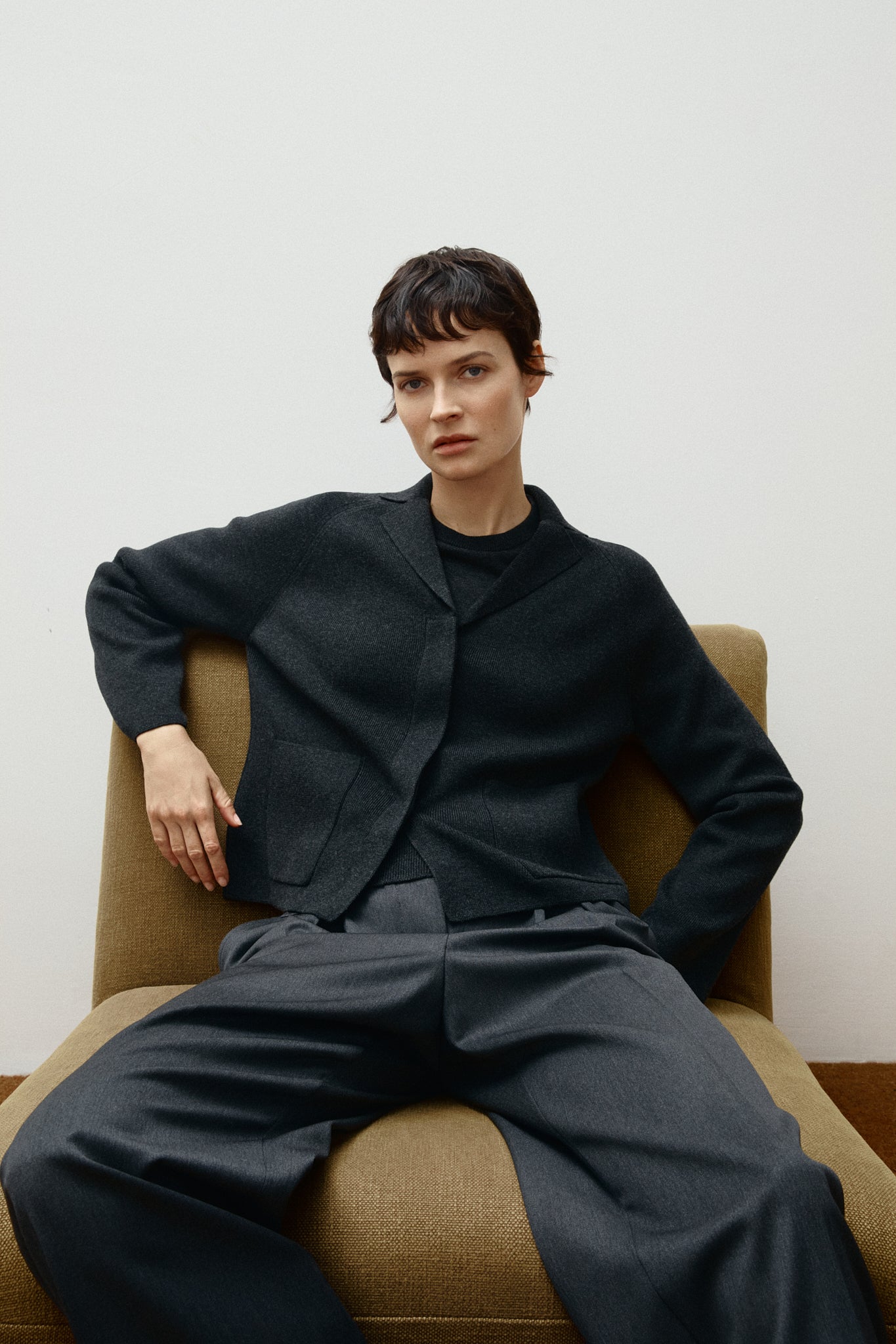 Person wearing amerino grey outfit sitting on a beige chair against a white wall