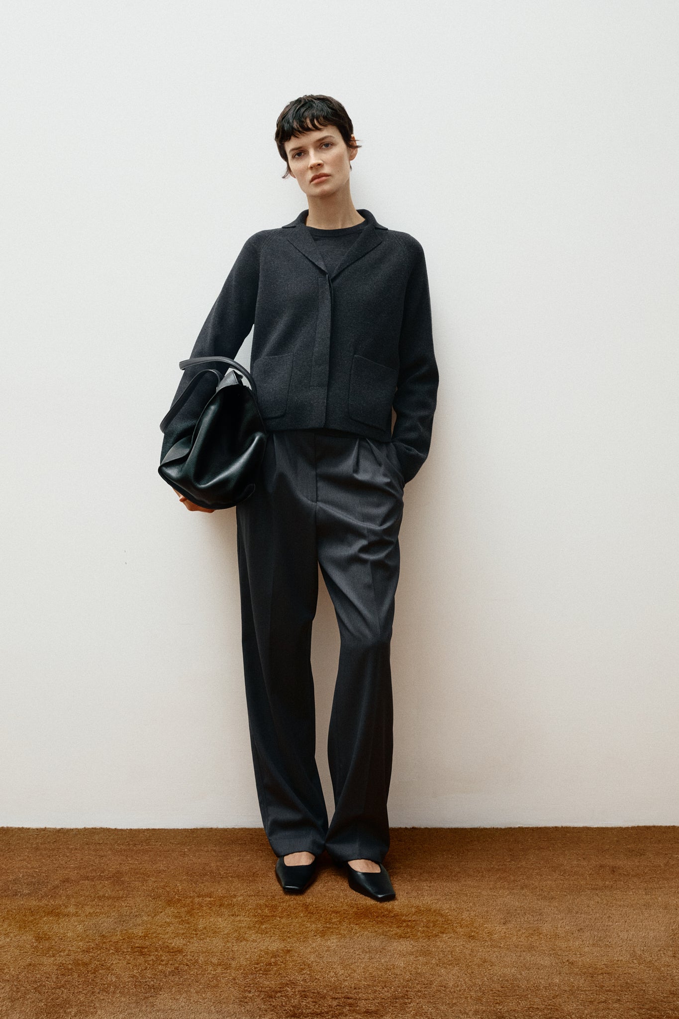 Woman wearing a grey wool jacket and dark gray pants on a white background