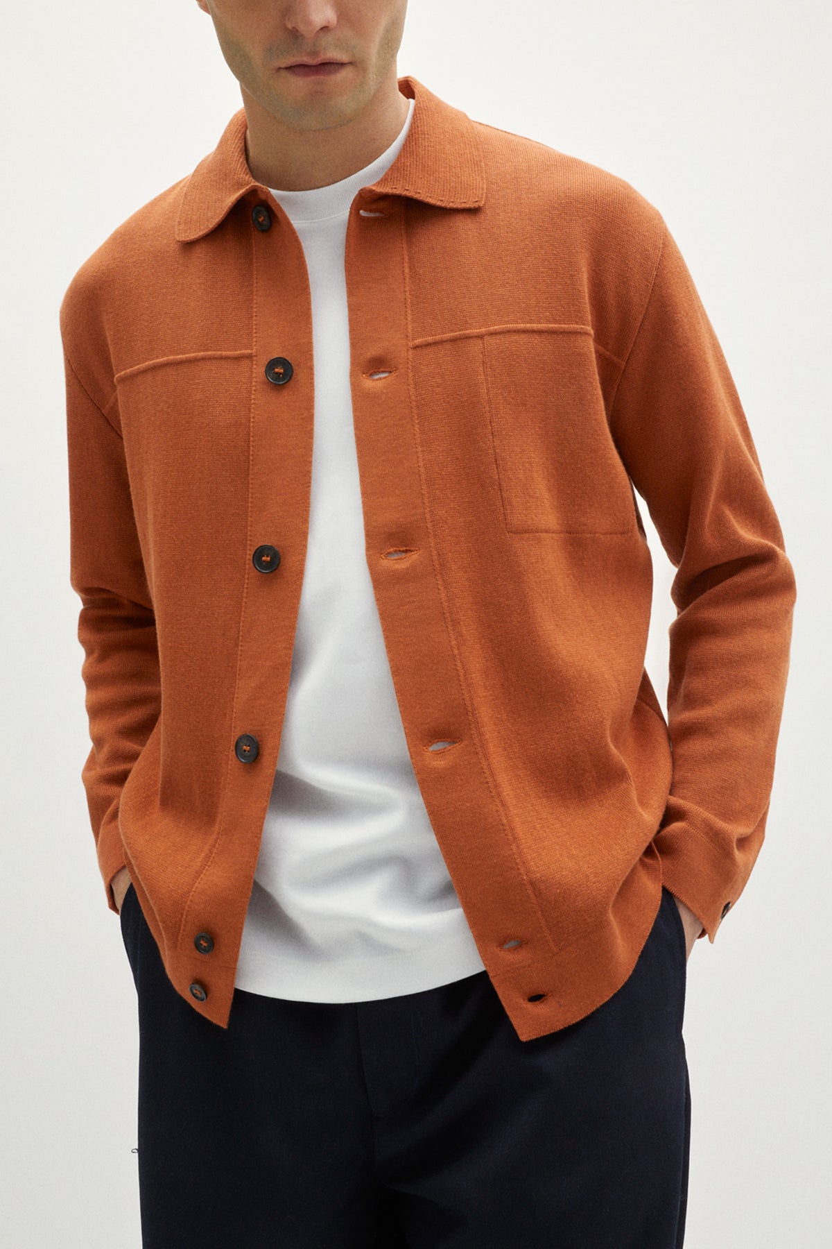 Person wearing an orange jacket over a white shirt with a plain background