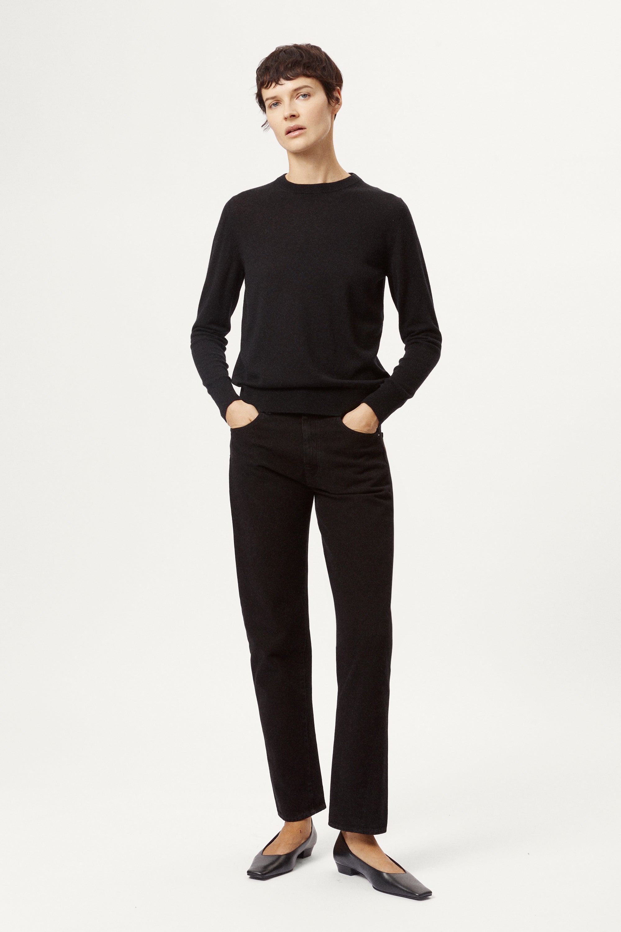 Person wearing a black sweater and black pants on a white background