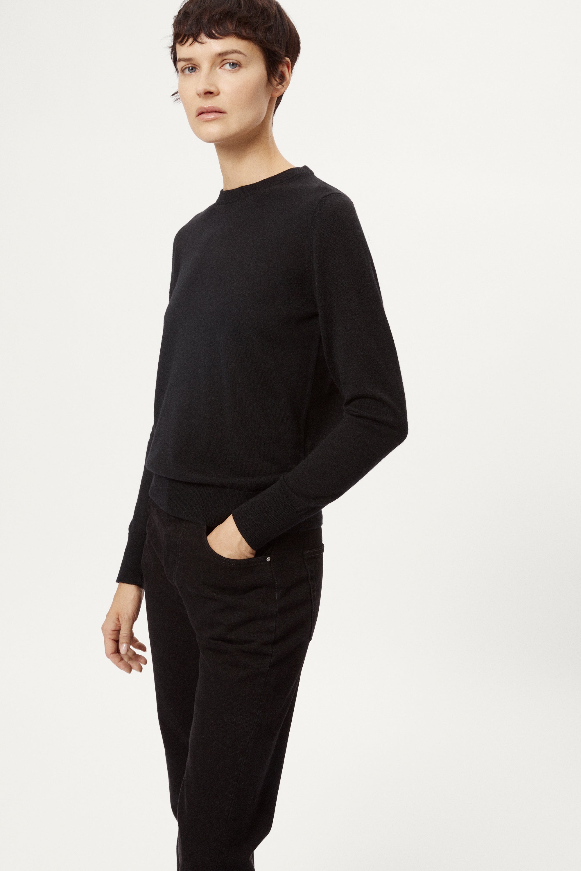 Person wearing a black sweater and black pants on a white background