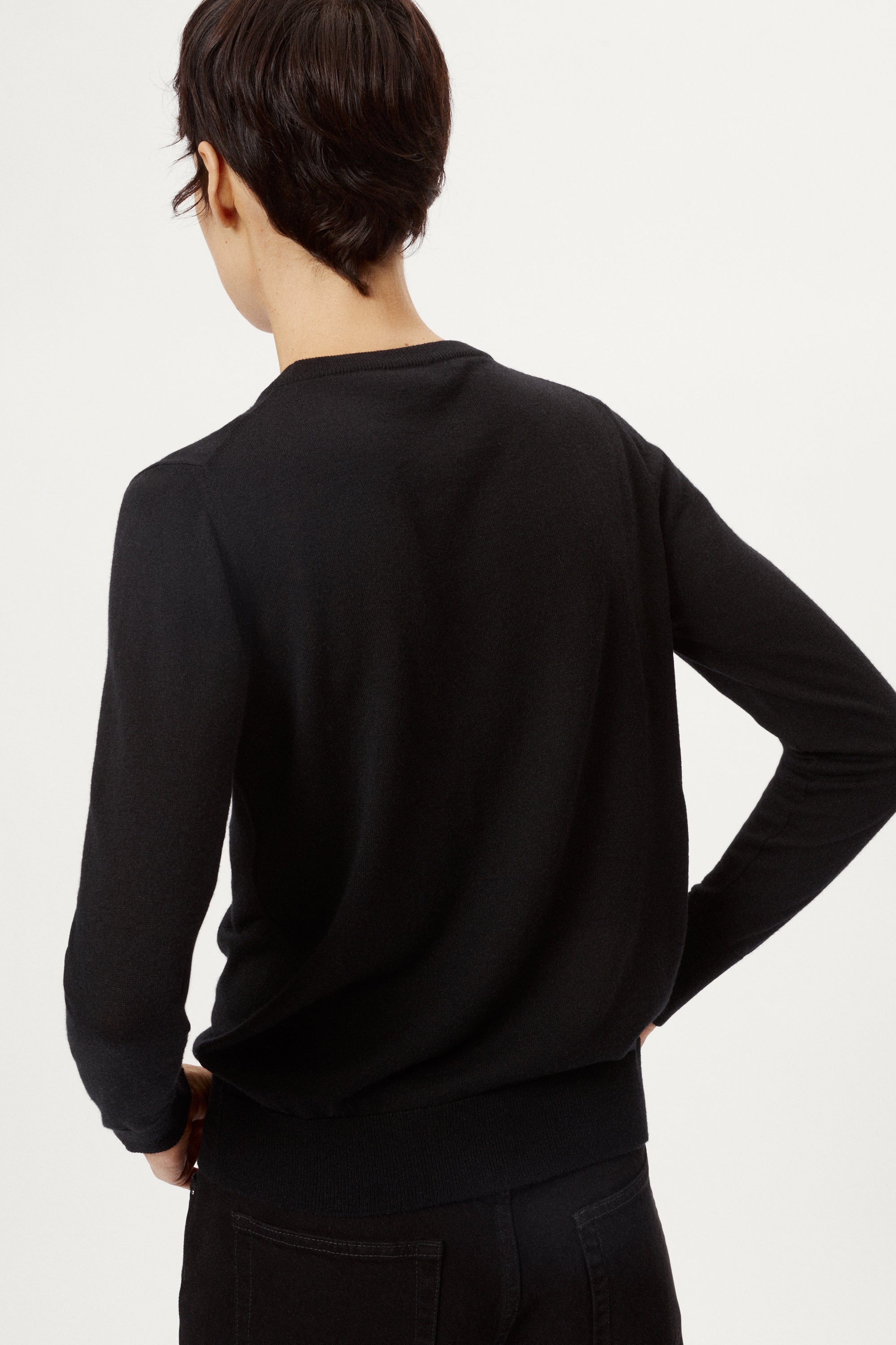 Person wearing a black sweater and black pants on a white background