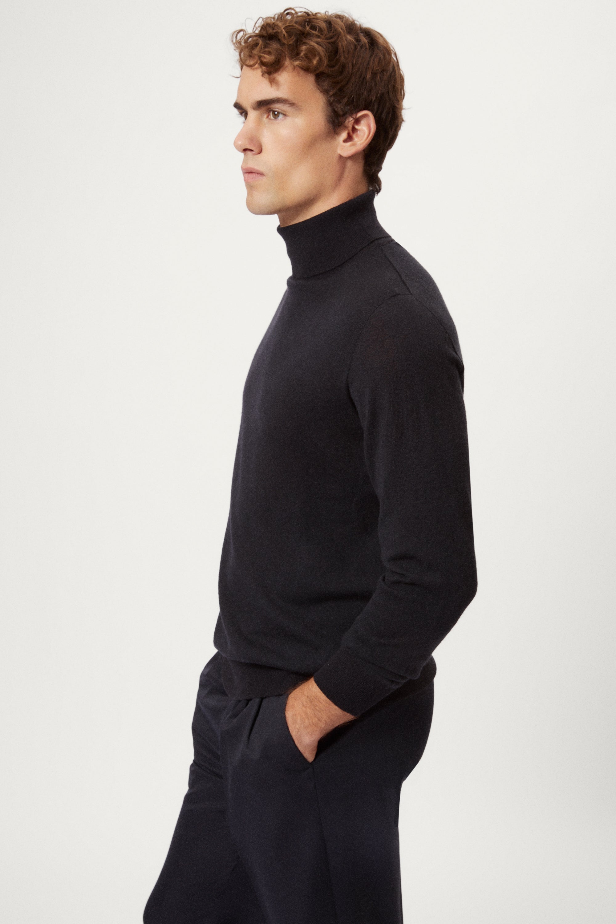 Man wearing a dark blue turtleneck sweater and pants on a white background