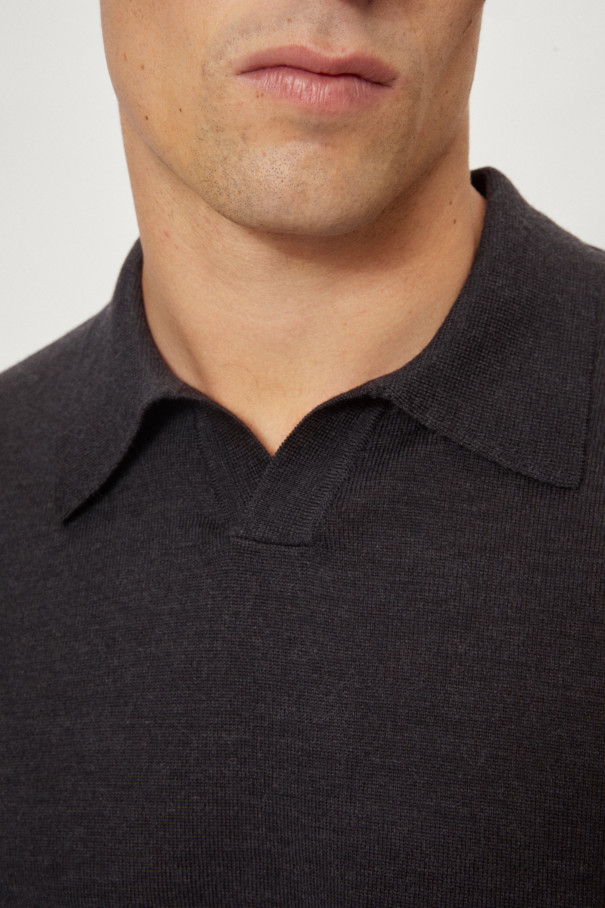 Man wearing a dark gray merino polo and black pants on a white background