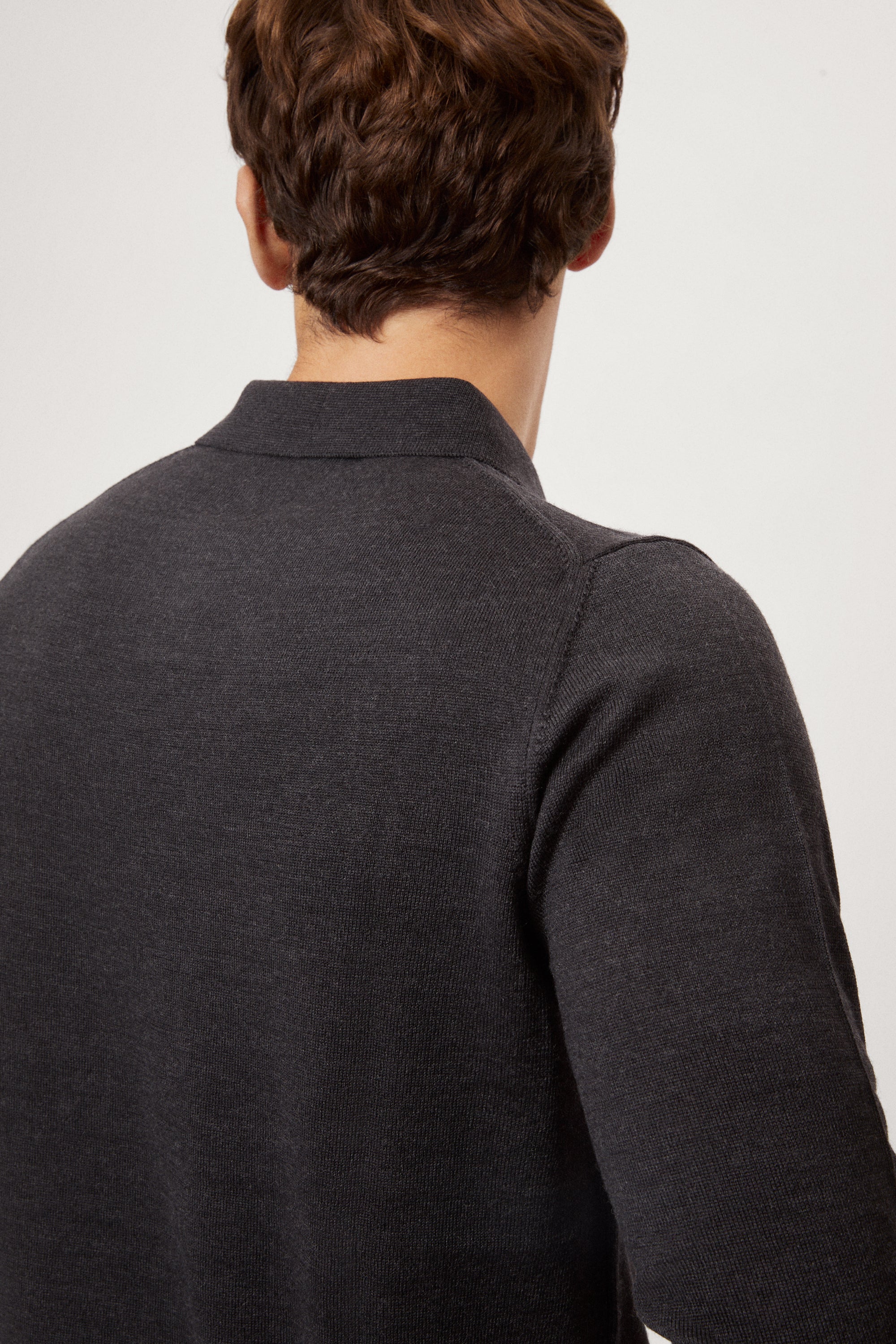 Man wearing a dark gray merino polo and black pants on a white background