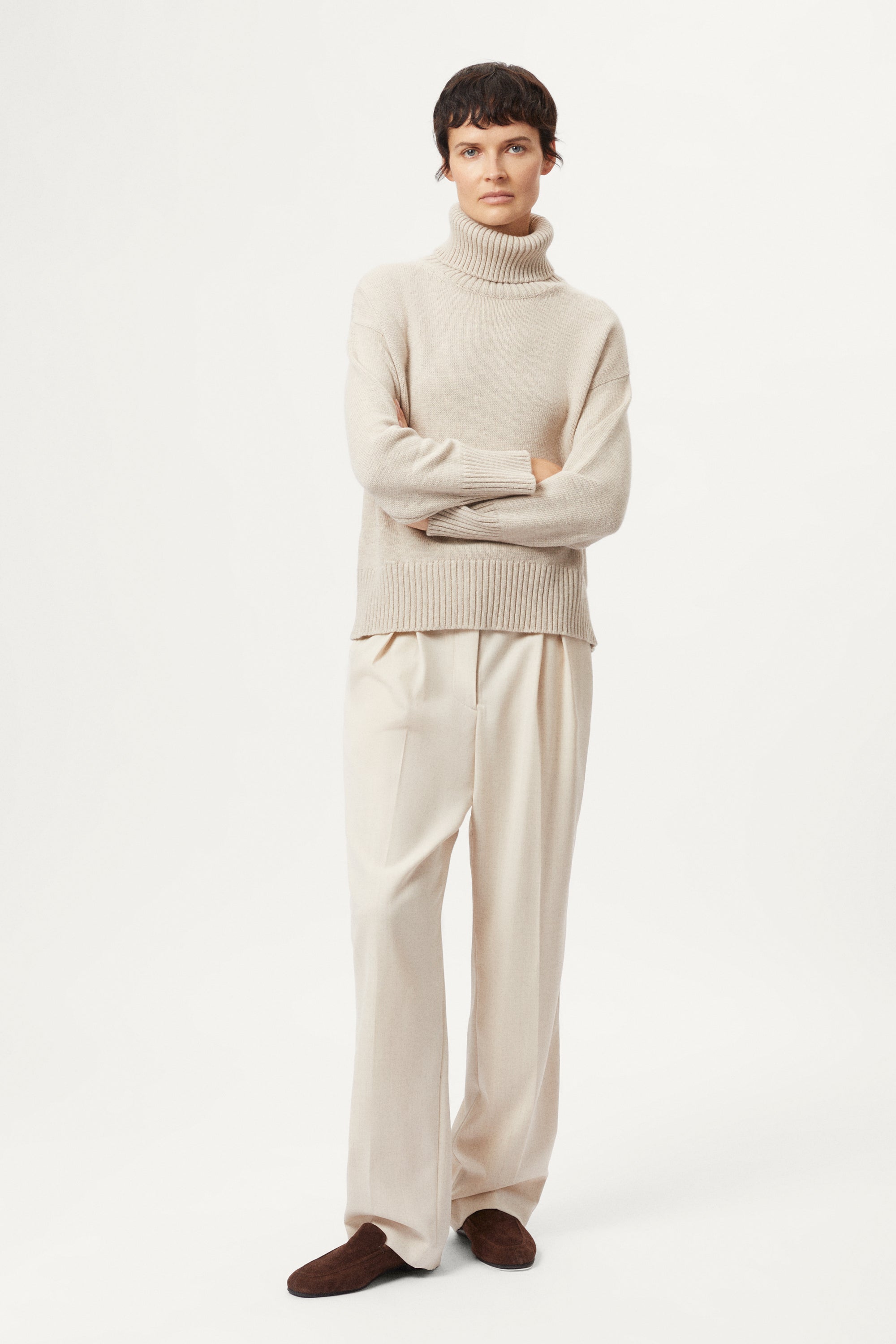 woman wearing a woolen beige sweater and wool pants on a white background