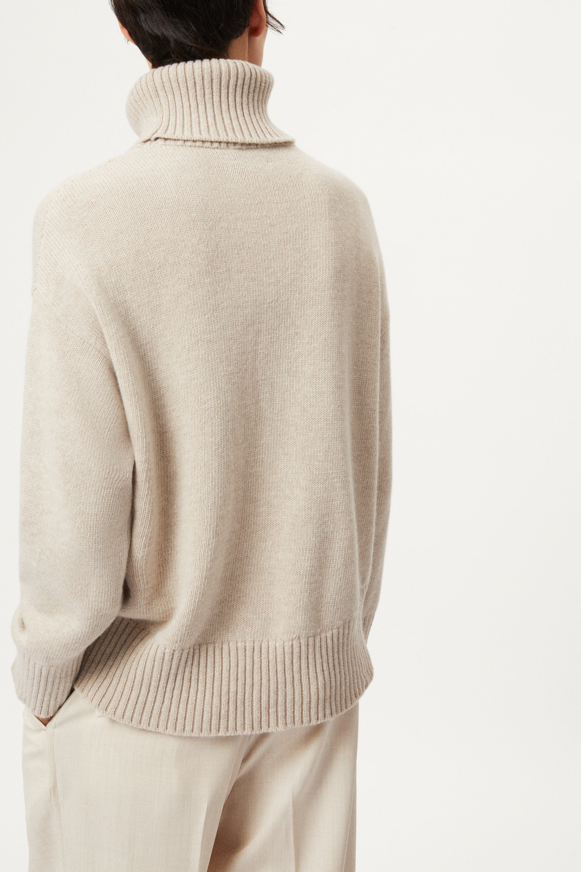 woman wearing a woolen beige sweater and wool pants on a white background