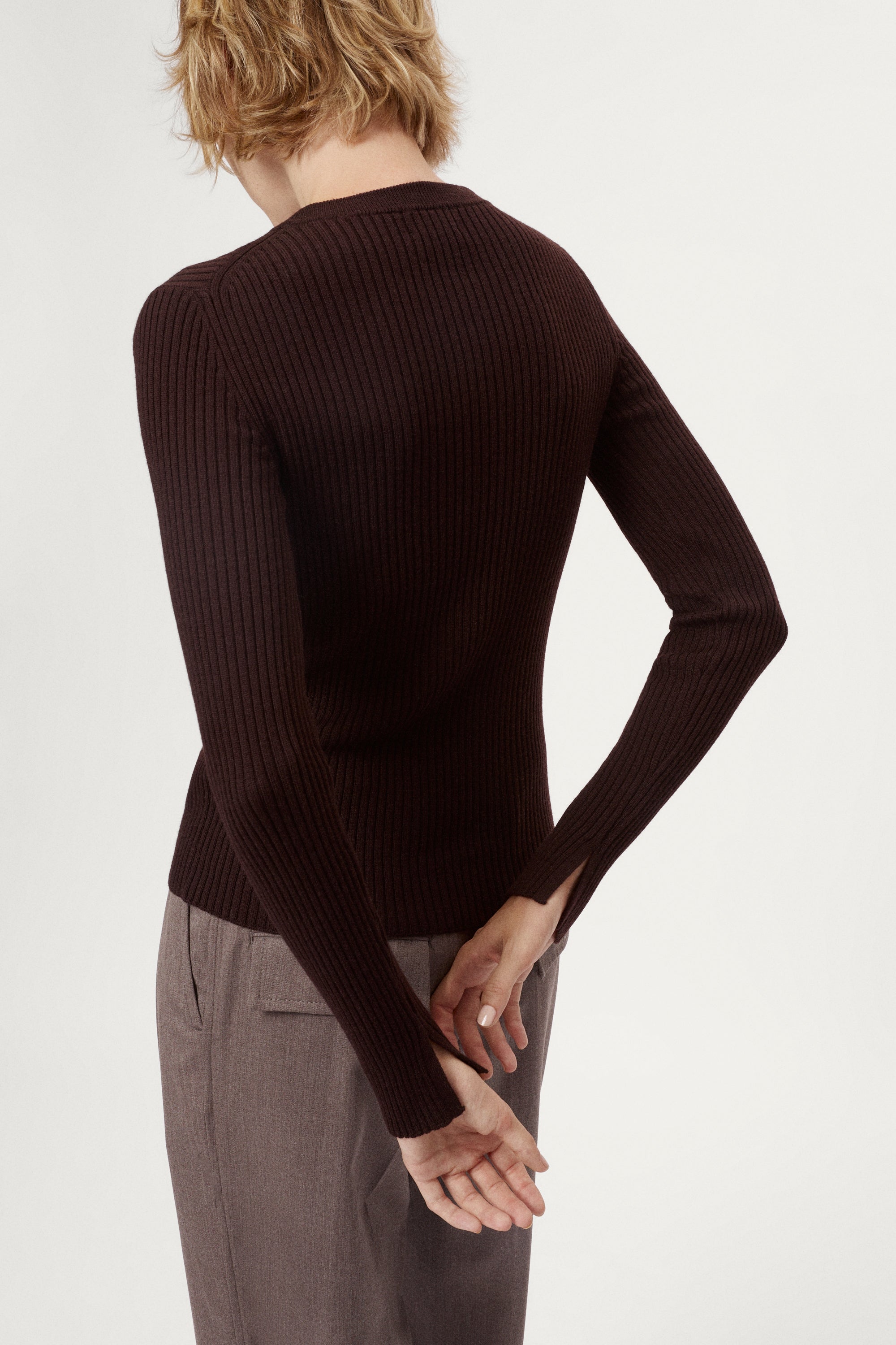 Woman wearing a dark brown sweater and light brown pleated pants on a white background