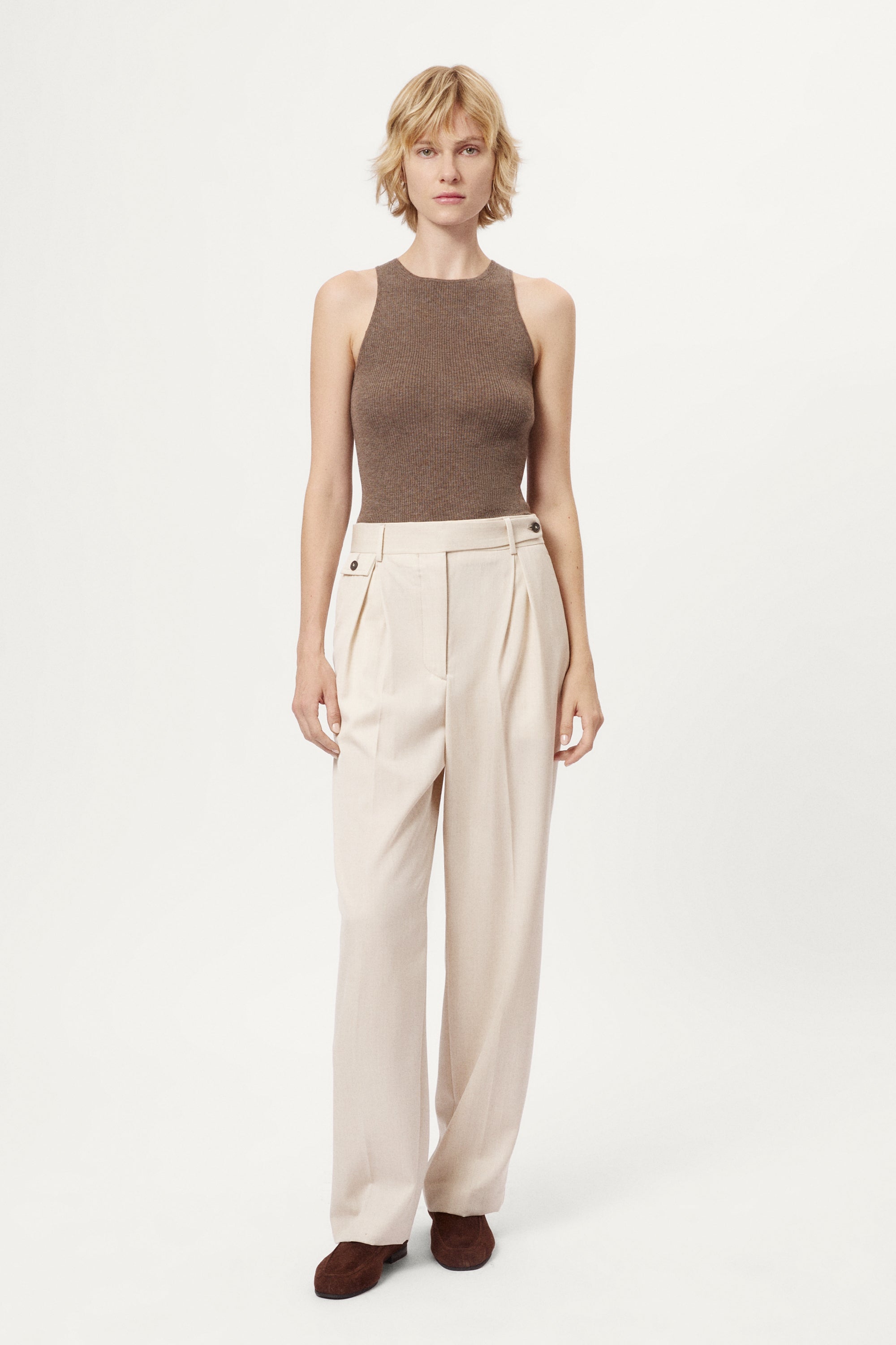 Woman wearing a brown sleeveless top and beige pants on a white background