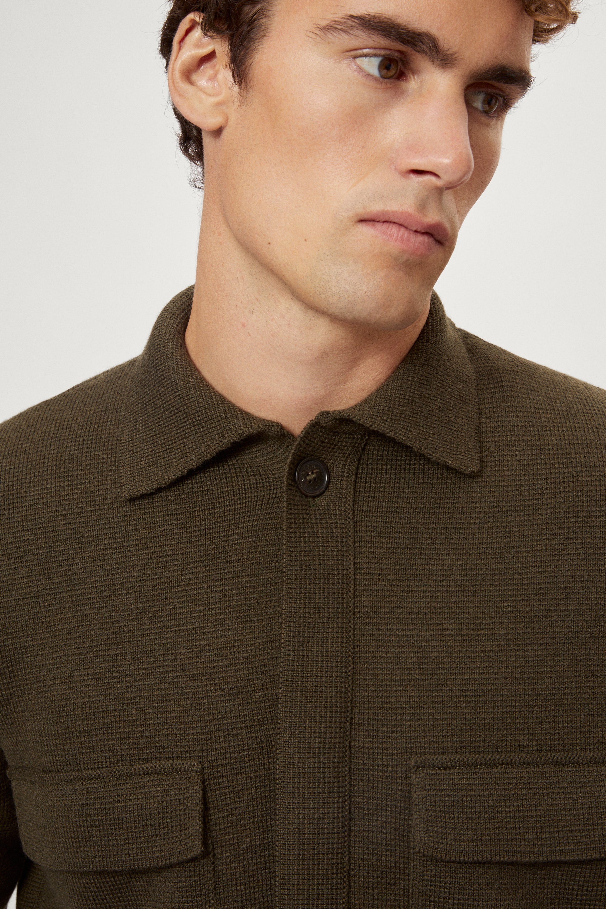 Man wearing a merino green jacket, white t-shirt and blue pants on a white background