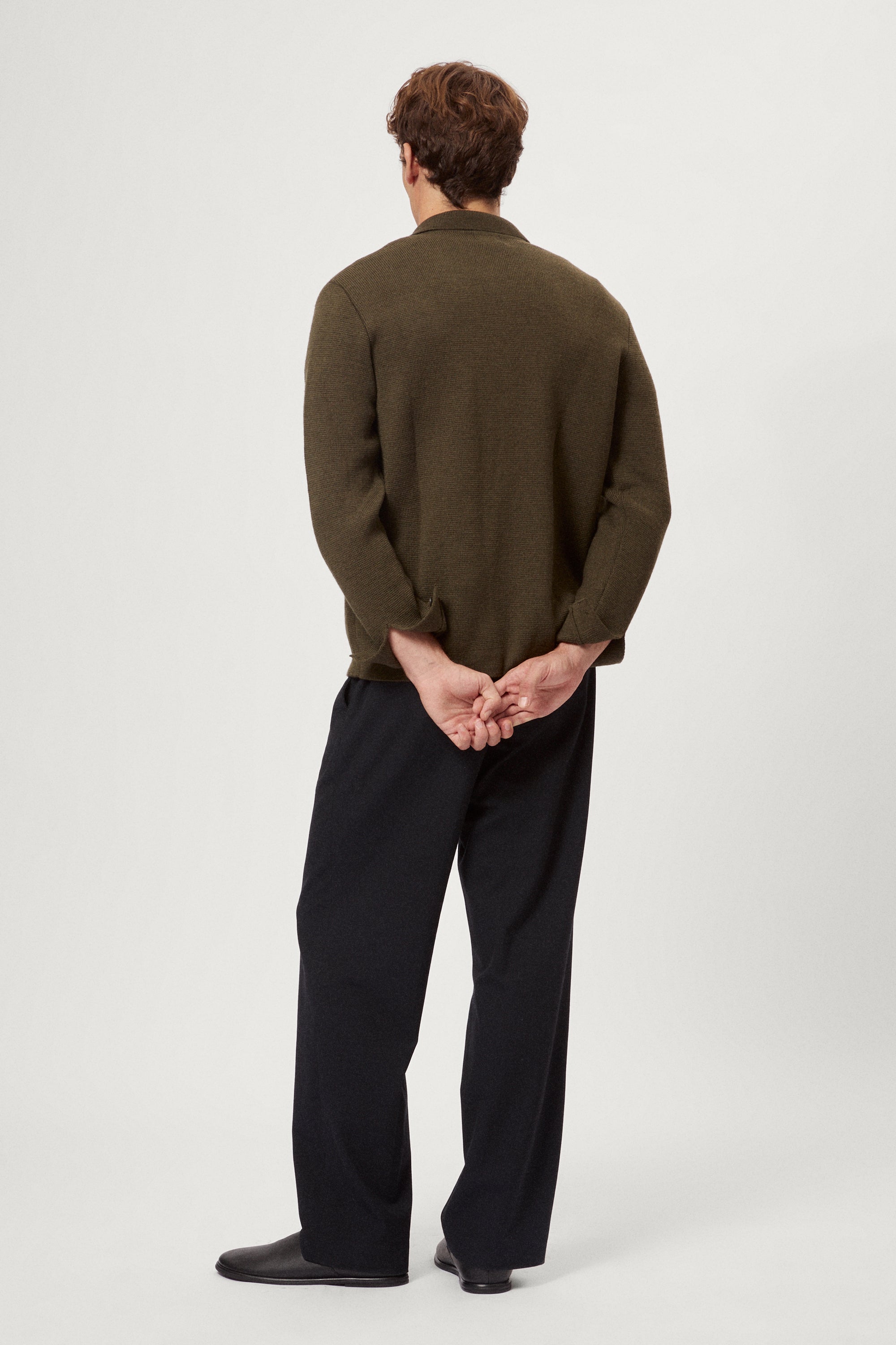 Man wearing a merino green jacket, white t-shirt and blue pants on a white background