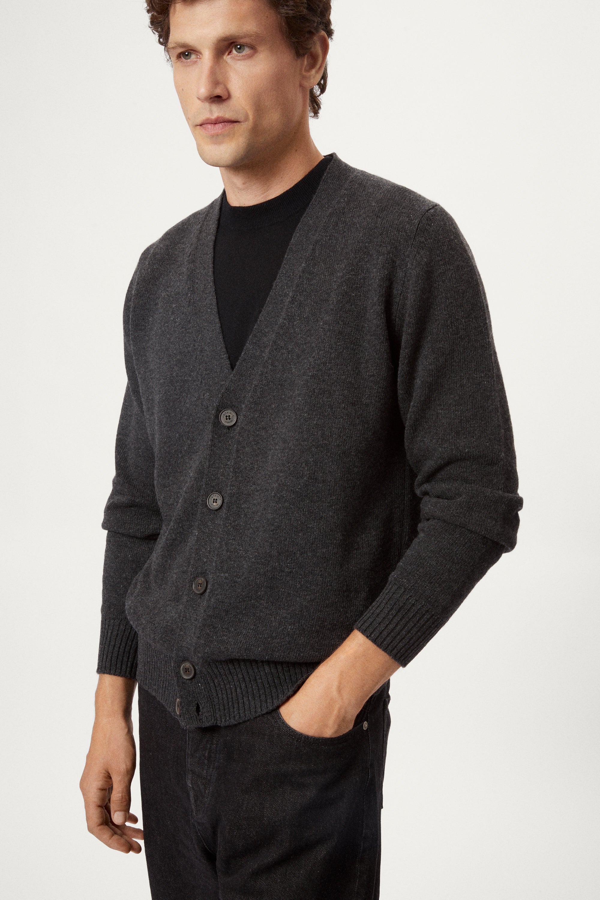 Man wearing a dark gray woolen cardigan over a black shirt on a white background