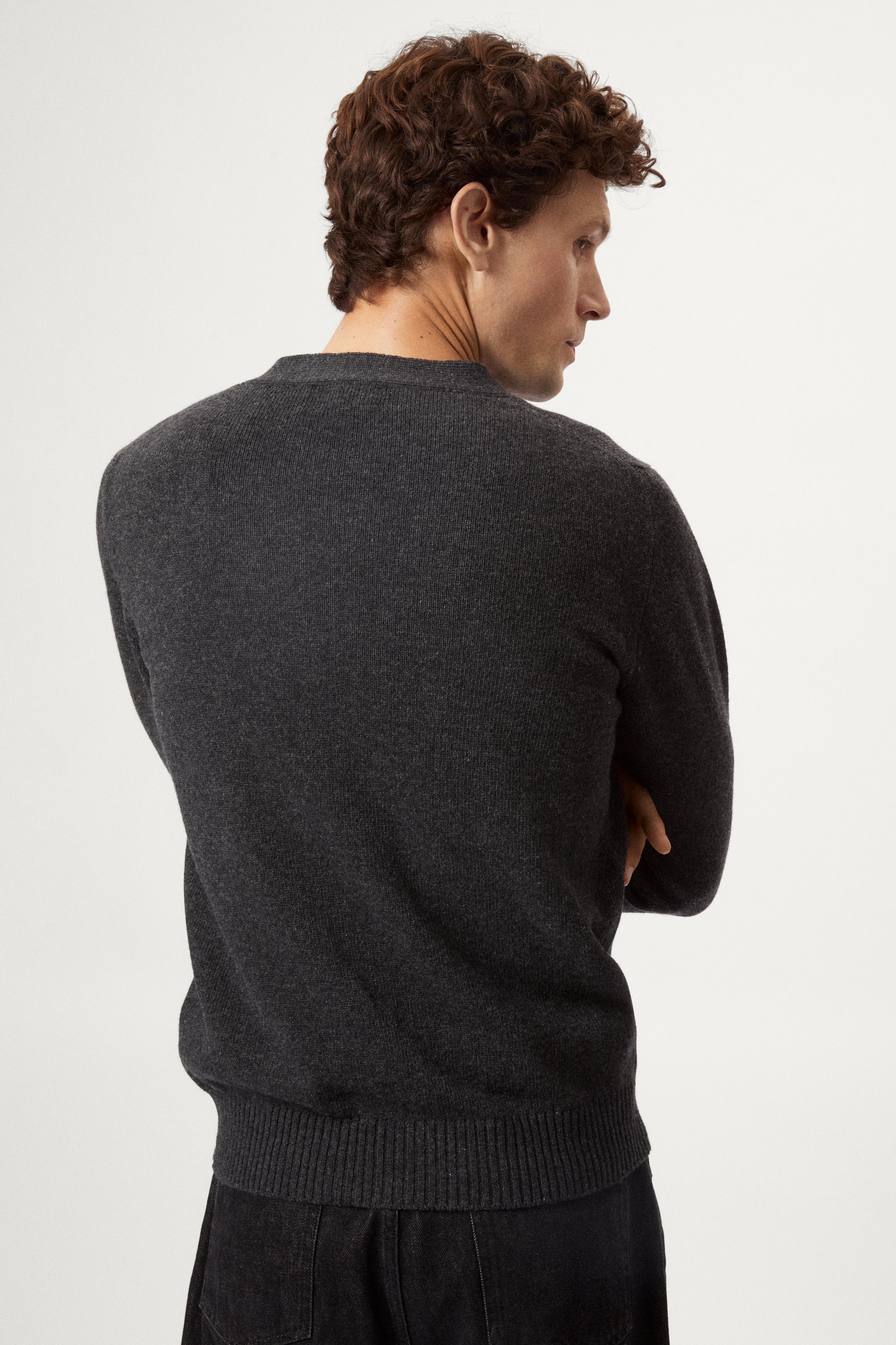Man wearing a dark gray woolen cardigan over a black shirt on a white background
