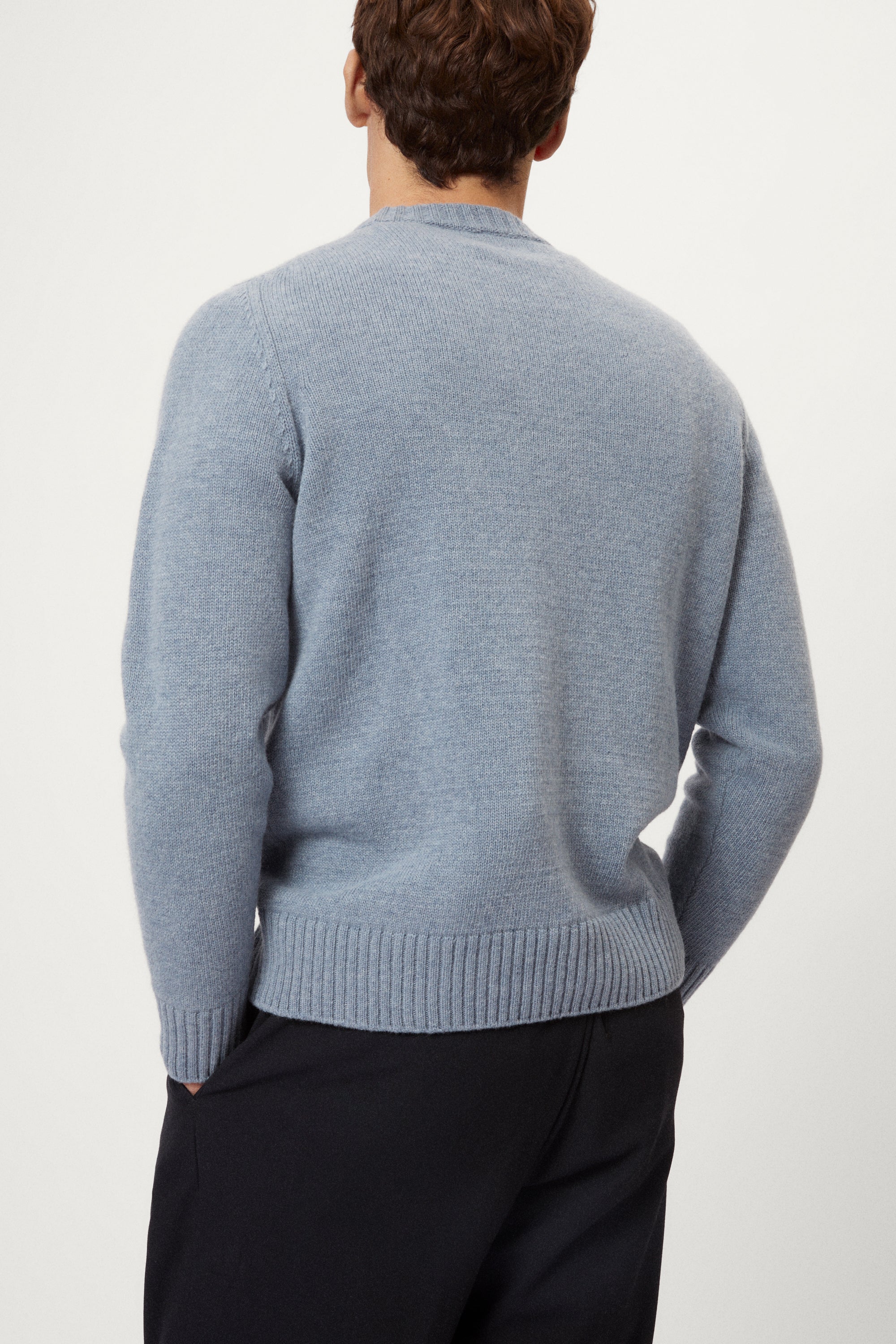 Man wearing a light blue woolen sweater and dark pants on a white background