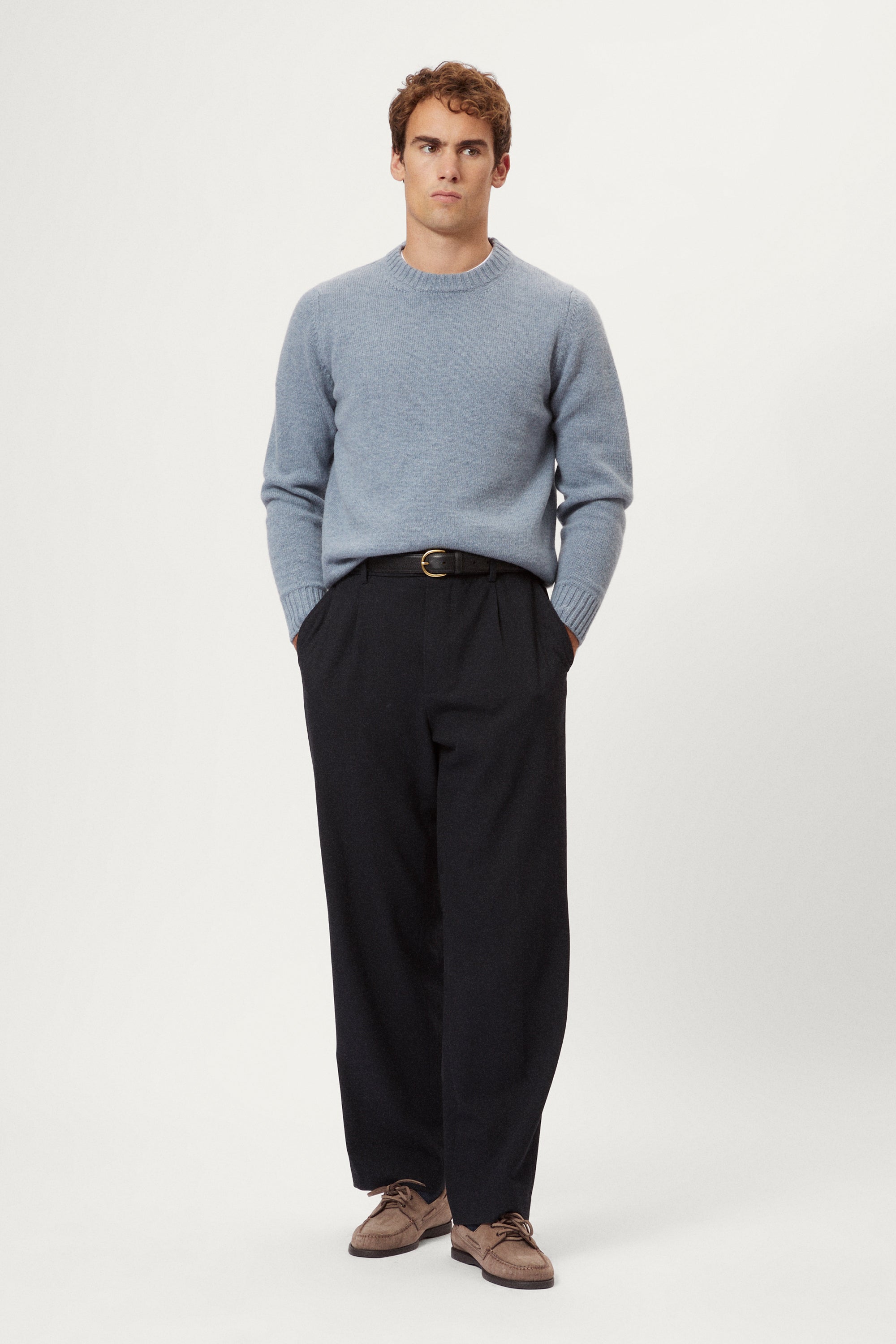 Man wearing a light blue woolen sweater and dark pants on a white background