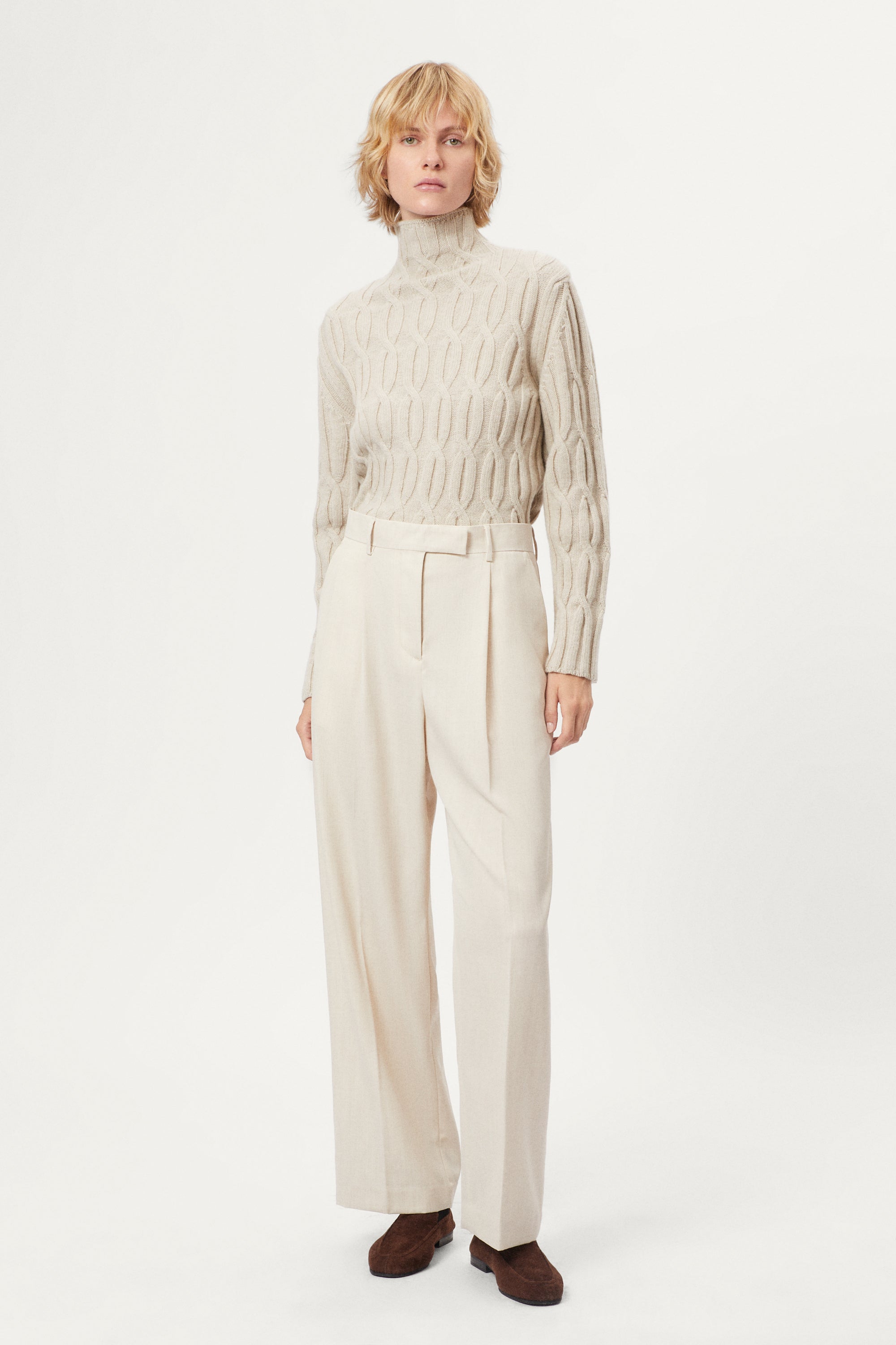 woman wearing a woolen beige cable knit turtleneck sweater on a white background