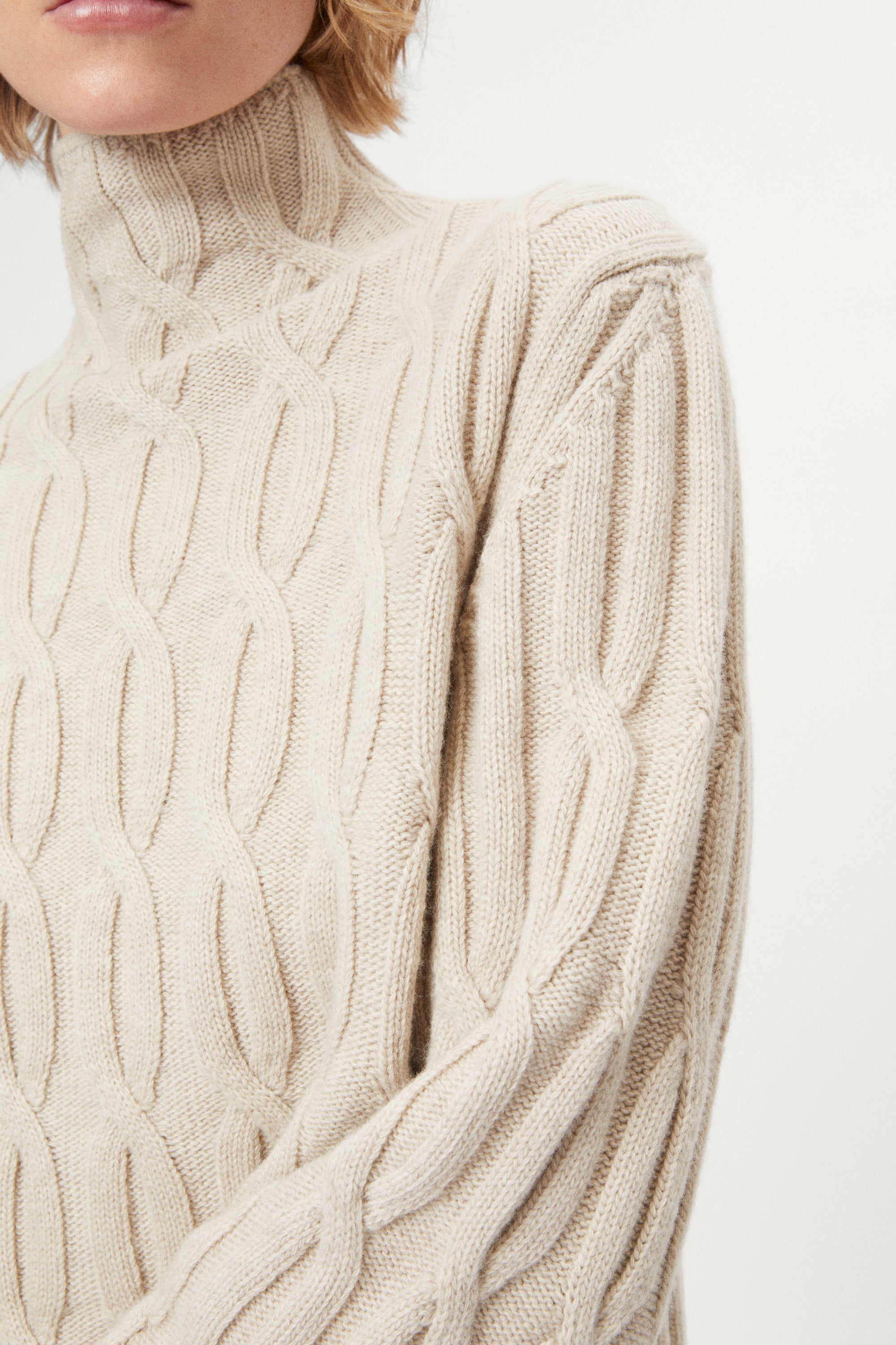 woman wearing a woolen beige cable knit turtleneck sweater on a white background