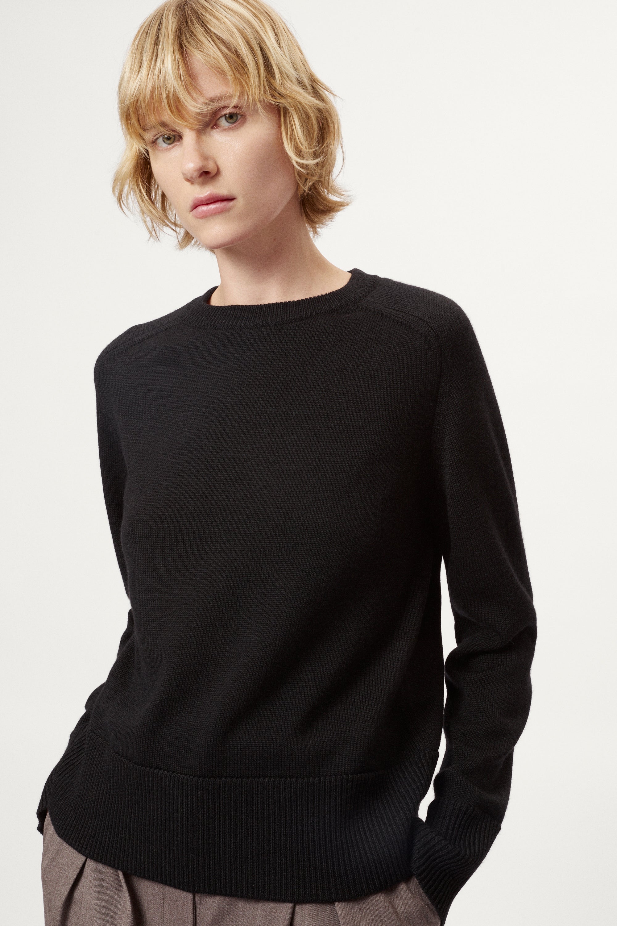Woman wearing a black merino sweater on a plain background