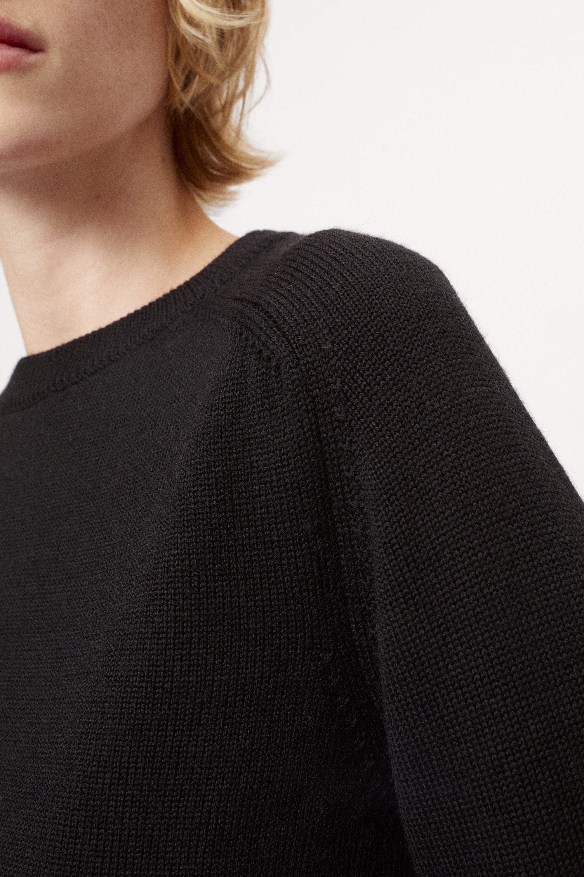 Woman wearing a black merino sweater on a plain background