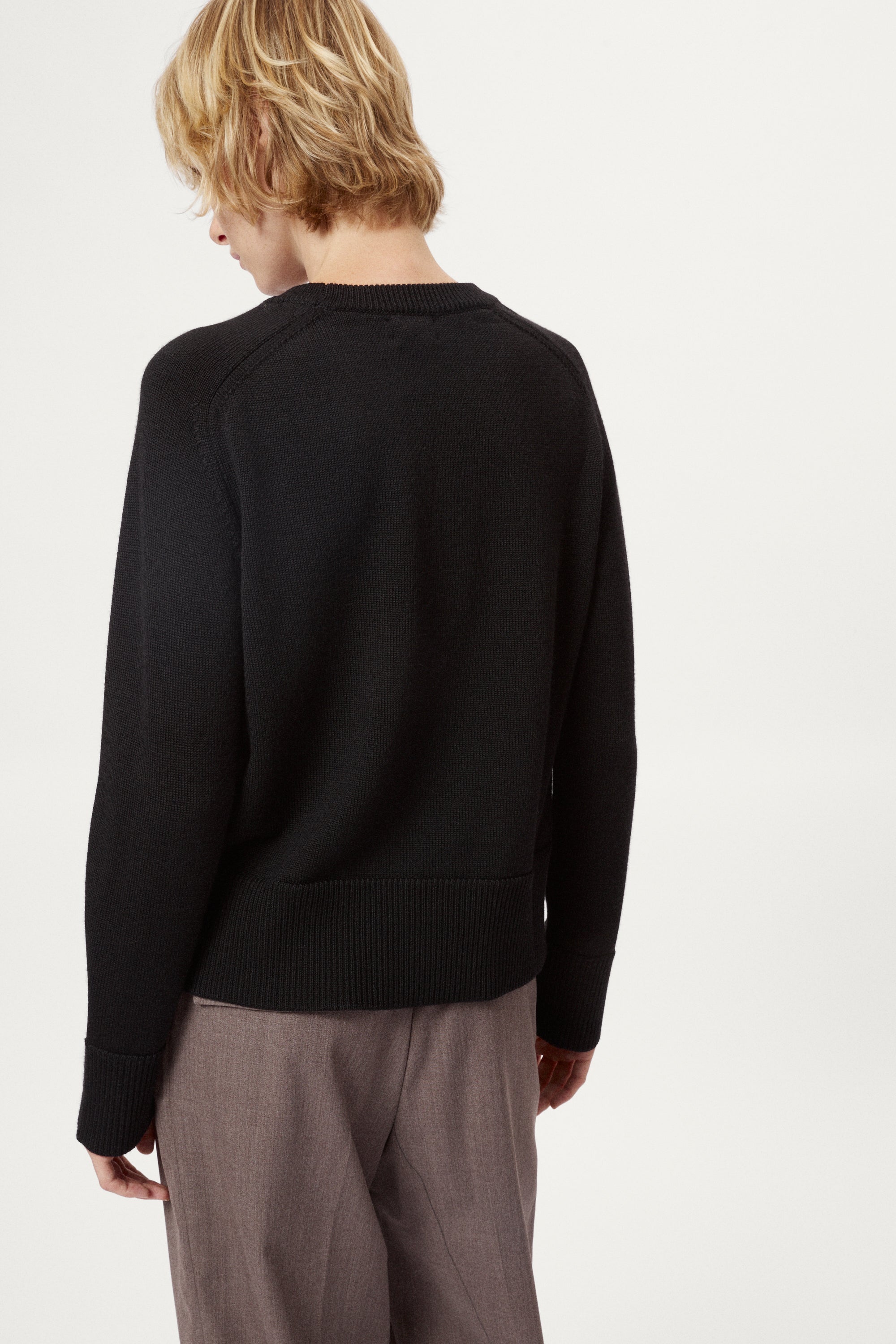Woman wearing a black merino sweater on a plain background