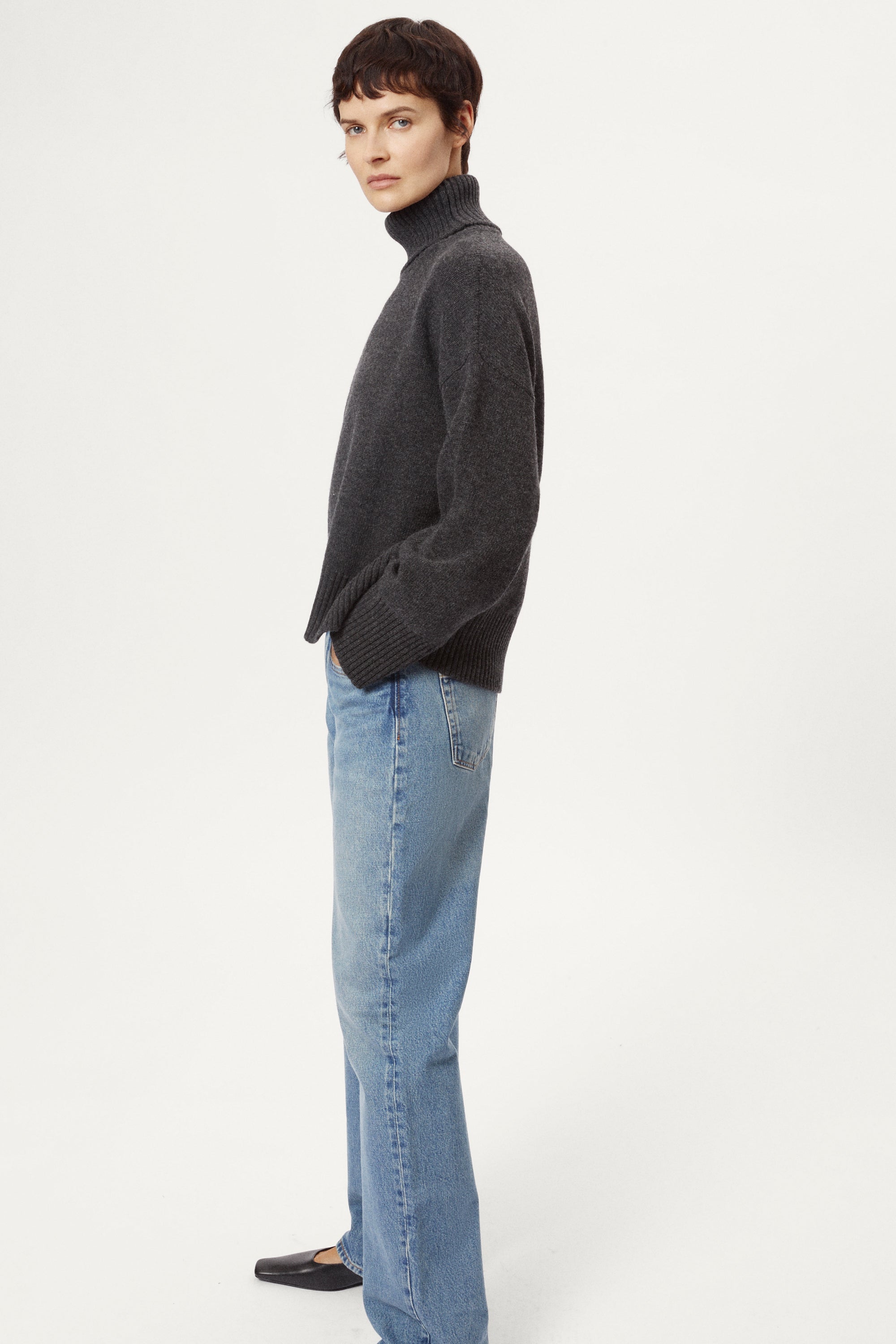 woman wearing a woolen dark grey turtleneck sweater and blue jeans on a white background
