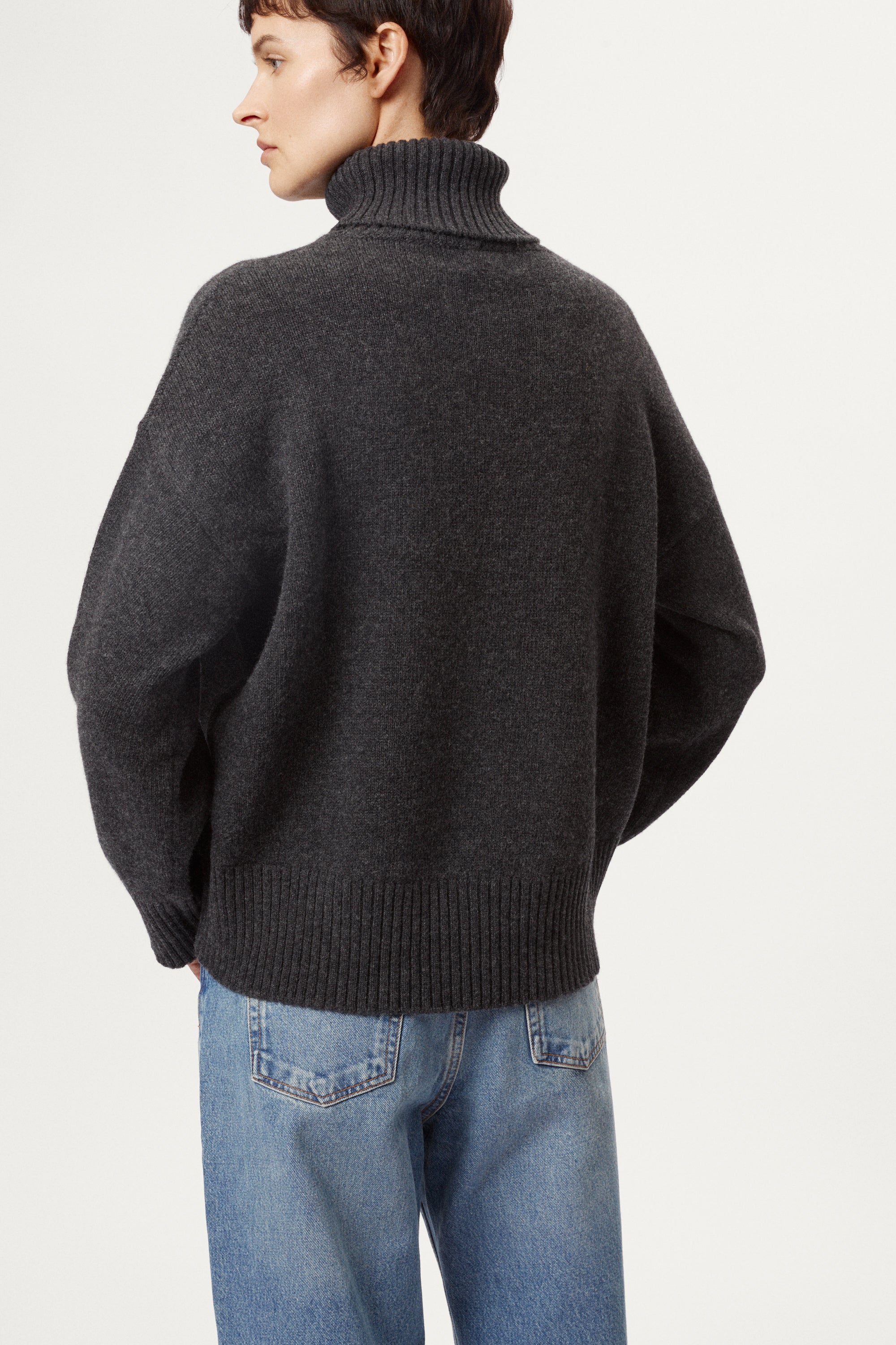woman wearing a woolen dark grey turtleneck sweater and blue jeans on a white background
