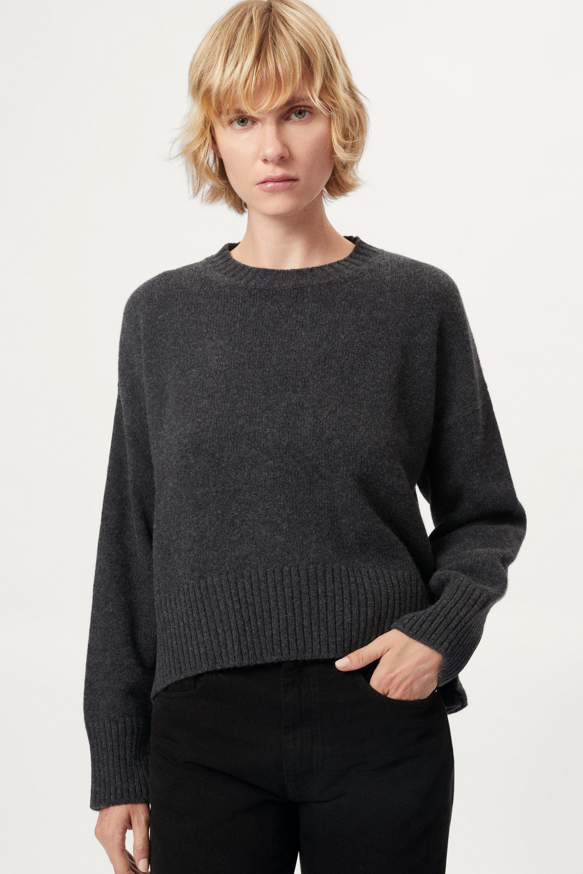 Woman wearing a woolen dark gray sweater and black pants on a white background