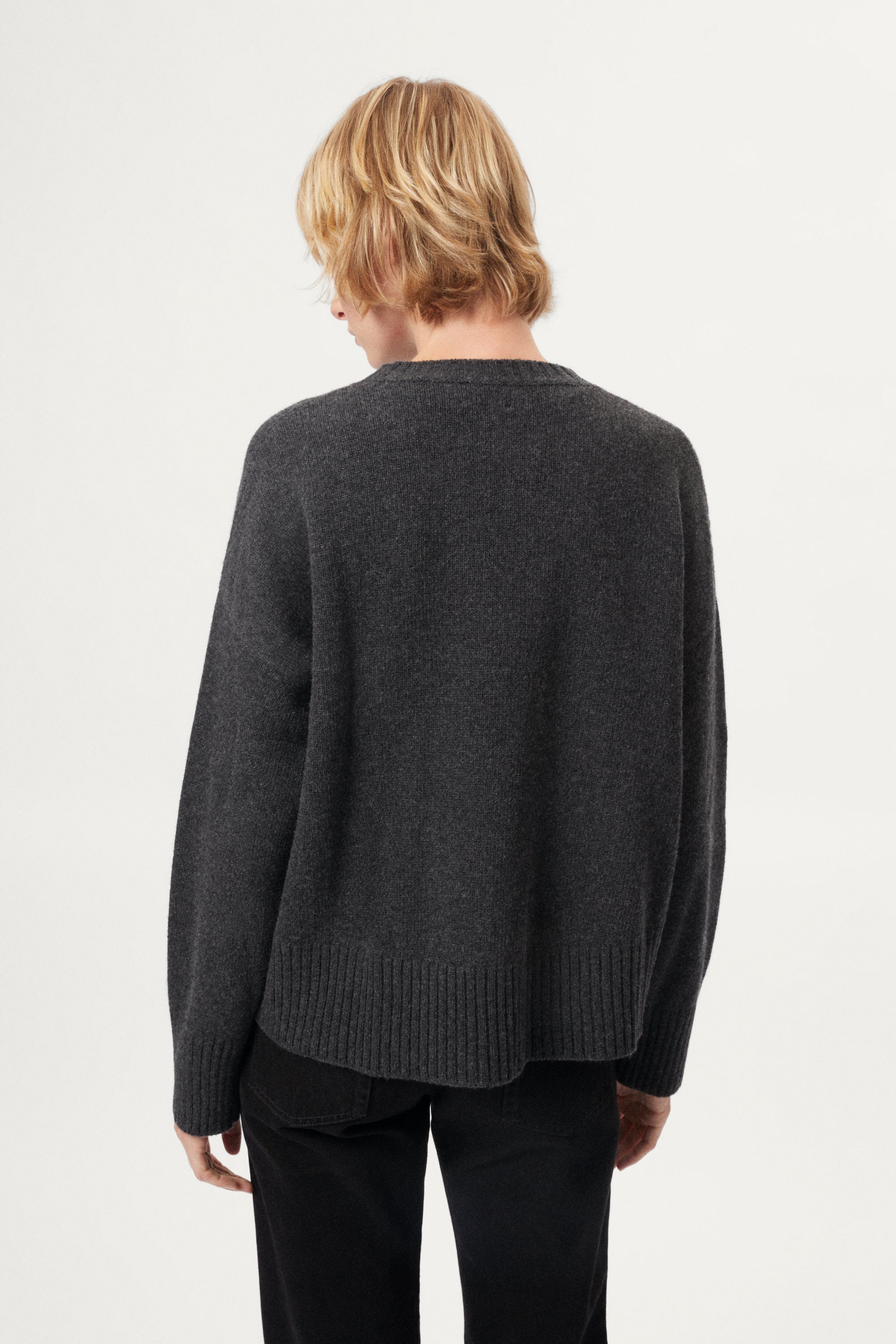 Woman wearing a woolen dark gray sweater and black pants on a white background