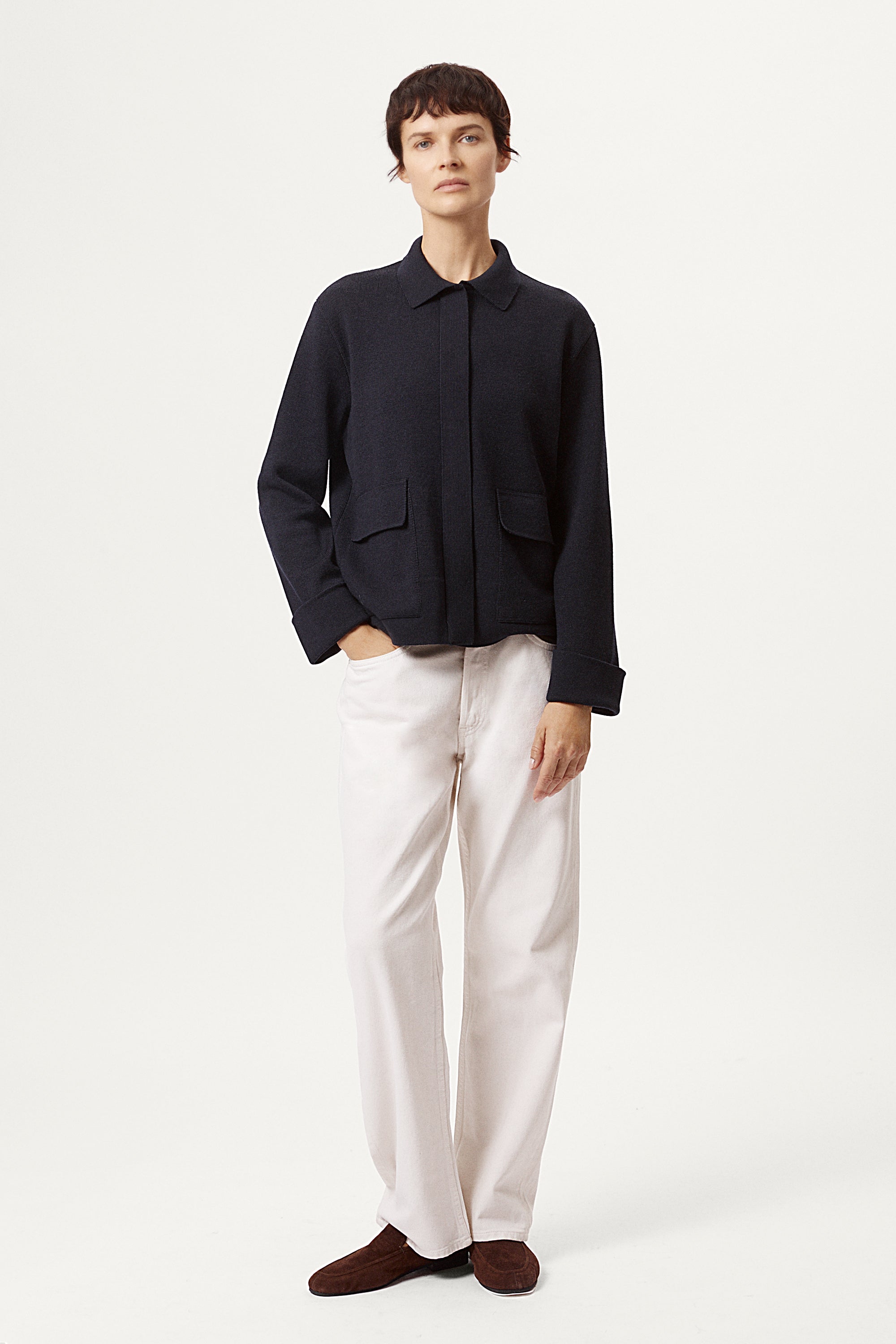 Woman wearing a blue jacket and white pants on a white background