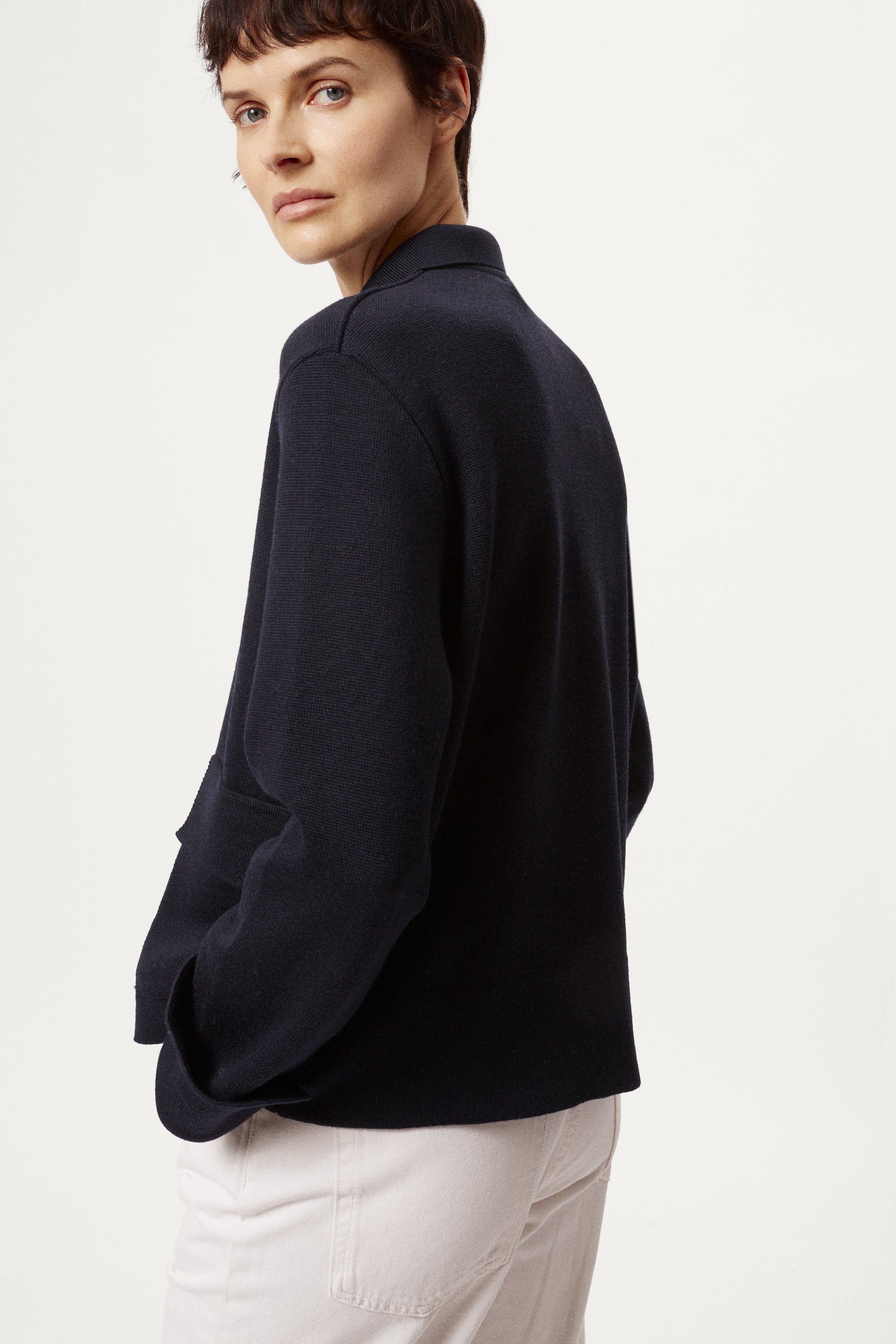 Woman wearing a blue jacket and white pants on a white background